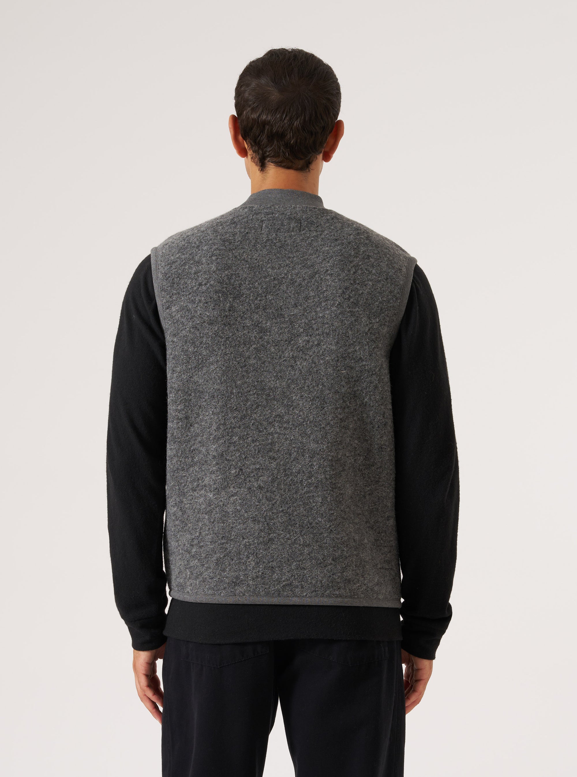 Back view of a model wearing a Grey Marl Wool Fleece Zip Waistcoat. The waistcoat is grey and made of wool fleece. The background is a plain white studio backdrop.
