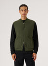 A man models the Olive Wool Fleece Zip Waistcoat against a white backdrop. The olive green waistcoat features a zip front and patch pockets.