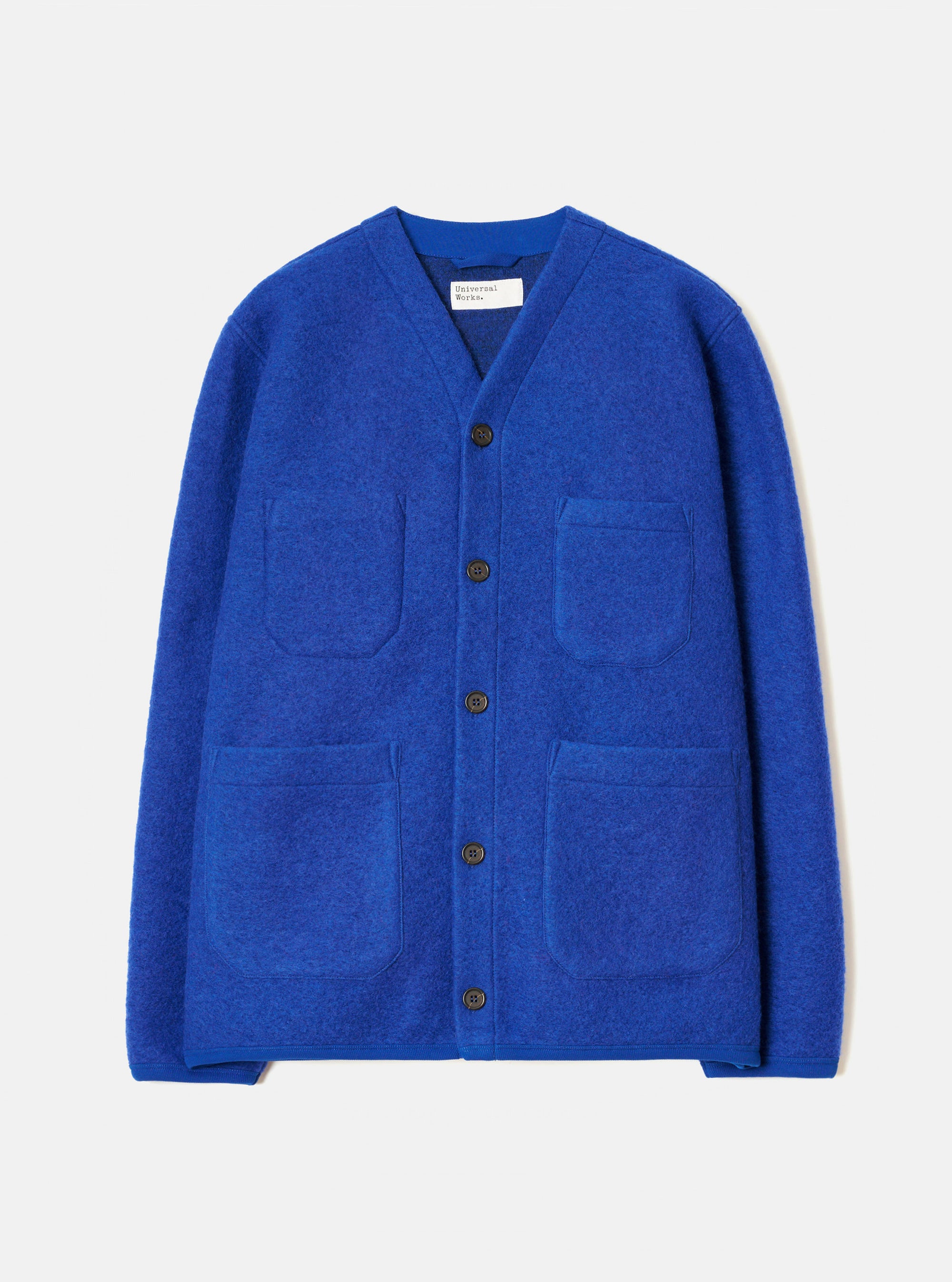 Blue wool fleece cardigan laid flat on a light grey studio backdrop. V-neckline with a branded woven label at the collar. Five dark horn buttons down the centre front. Two chest patch pockets and two larger patch pockets at the hem. Brushed wool fleece texture throughout. Straight hem and long sleeves with no cuffs.