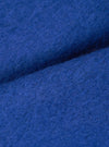 Close-up fabric detail of the blue wool fleece cardigan, showing the dense, brushed texture of the cobalt blue wool. Fine fibres are visible across the surface, with soft folds creating depth and shadow across the frame.