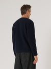 A man stands against a white background, modeling the Navy Wool Fleece Cardigan. The cardigan is a deep navy color and appears soft. He wears dark trousers.