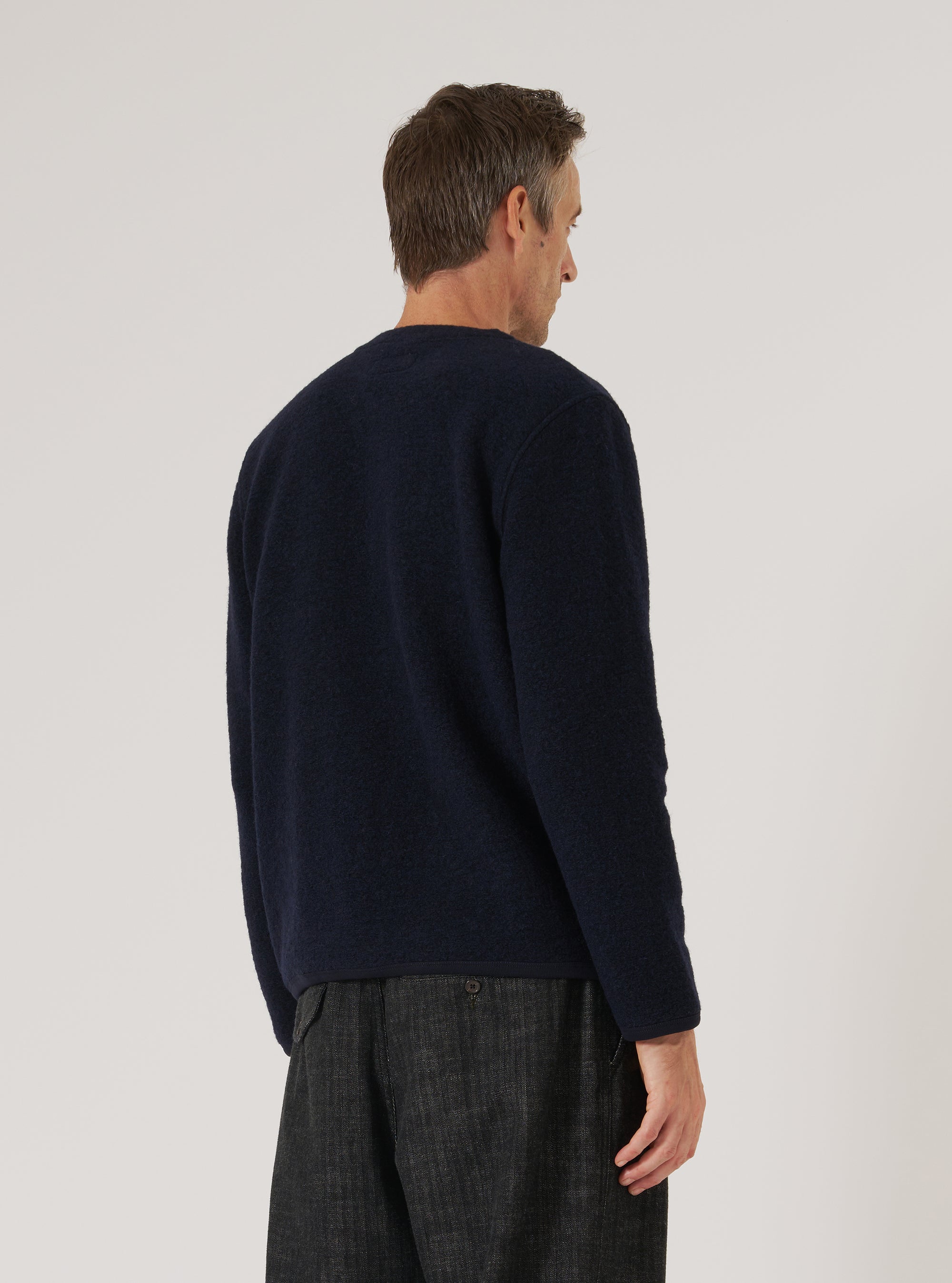 A man stands against a white background, modeling the Navy Wool Fleece Cardigan. The cardigan is a deep navy color and appears soft. He wears dark trousers.