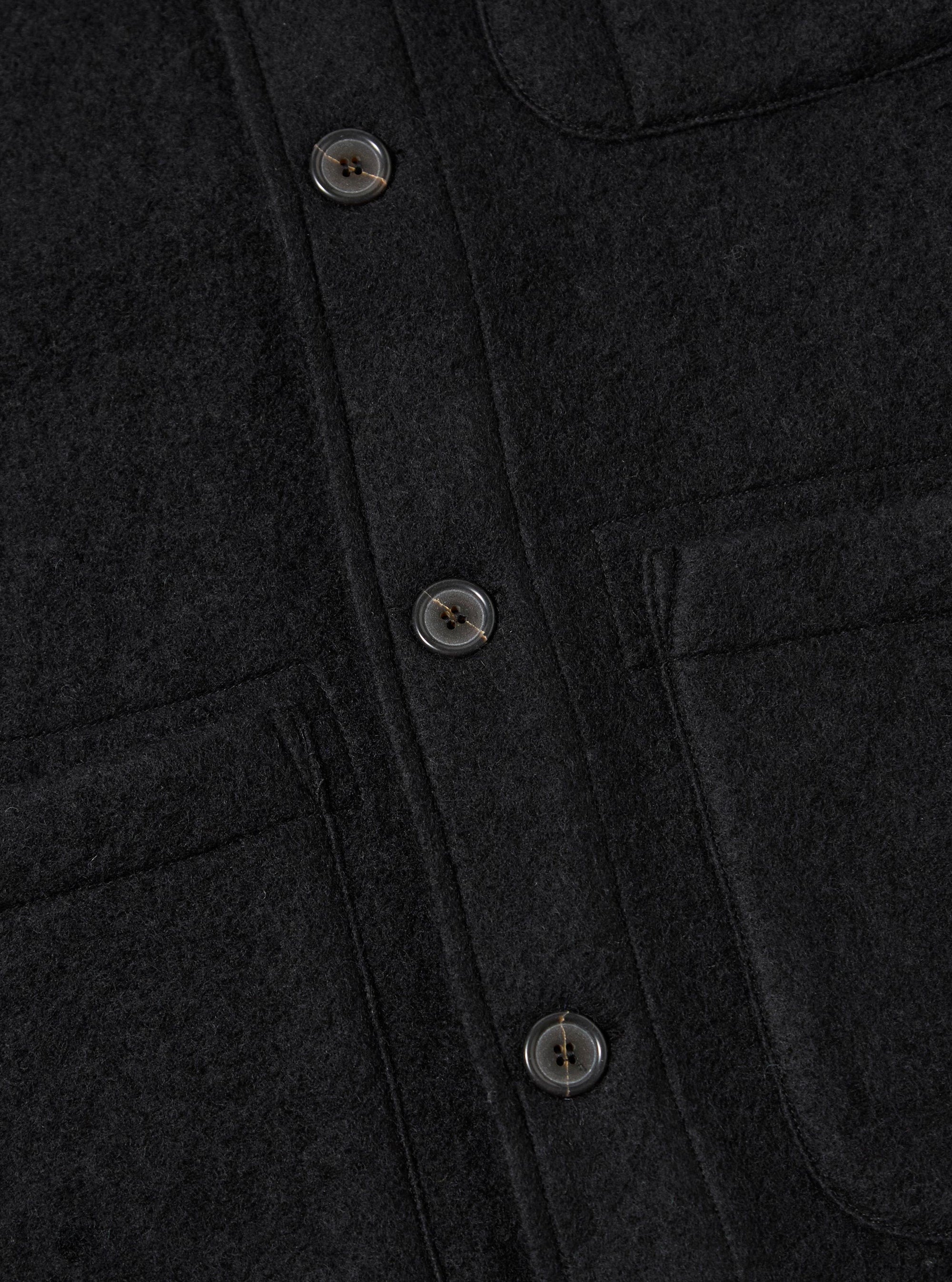 Close-up of the Black Wool Fleece Field Jacket showing the texture of the black wool fleece and button details. The jacket is neatly laid out on a flat surface.