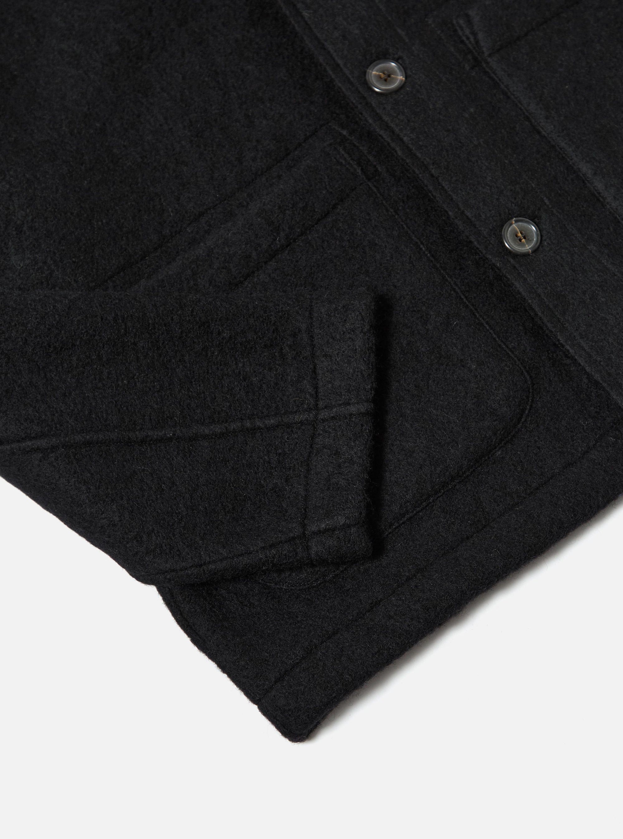 Close-up of the Black Wool Fleece Field Jacket on a white surface. Shows the texture, pockets, buttons, and construction details.
