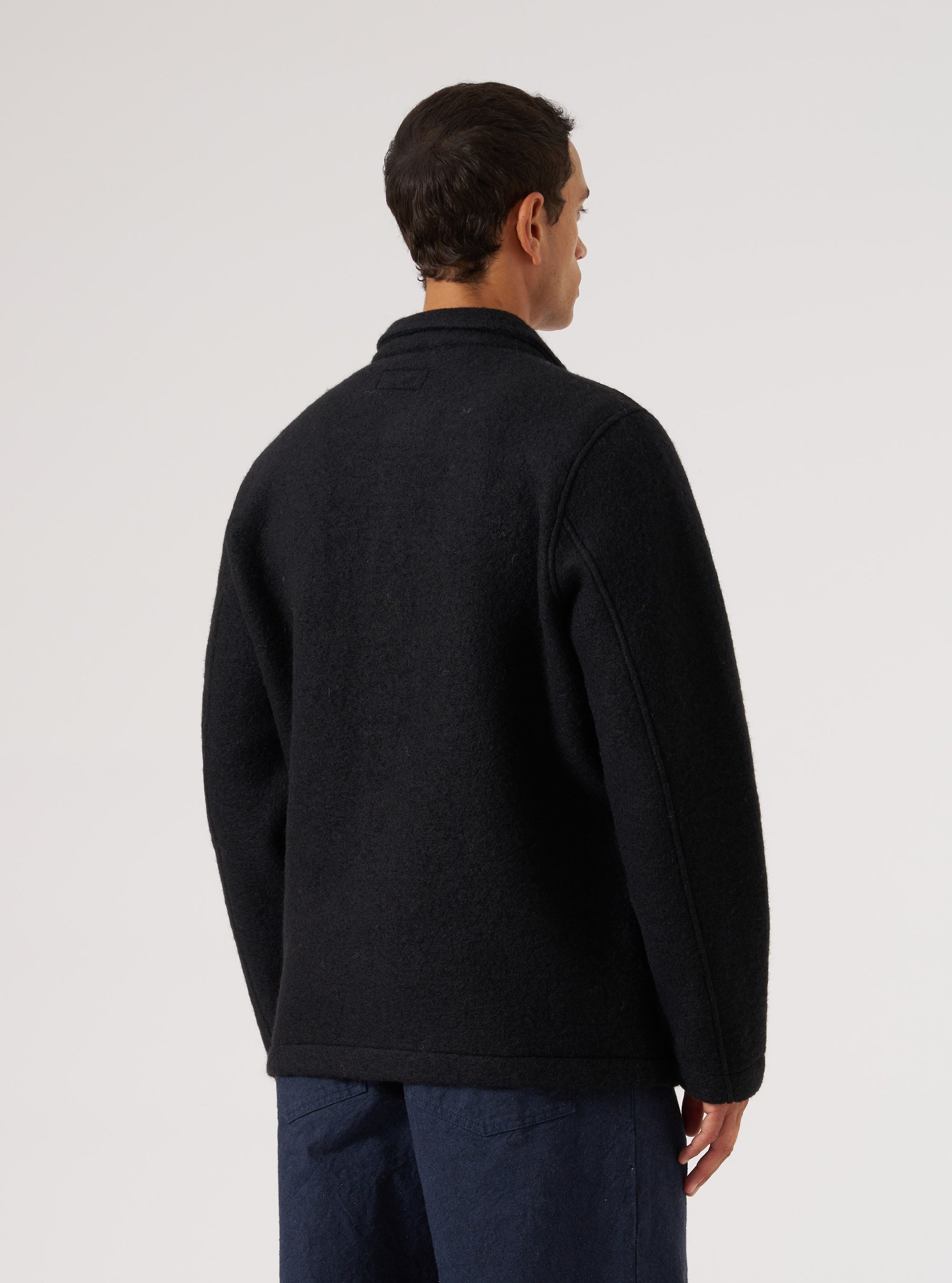 Back view of a man wearing a Black Wool Fleece Field Jacket. The jacket is on a white background and the model is wearing blue pants.