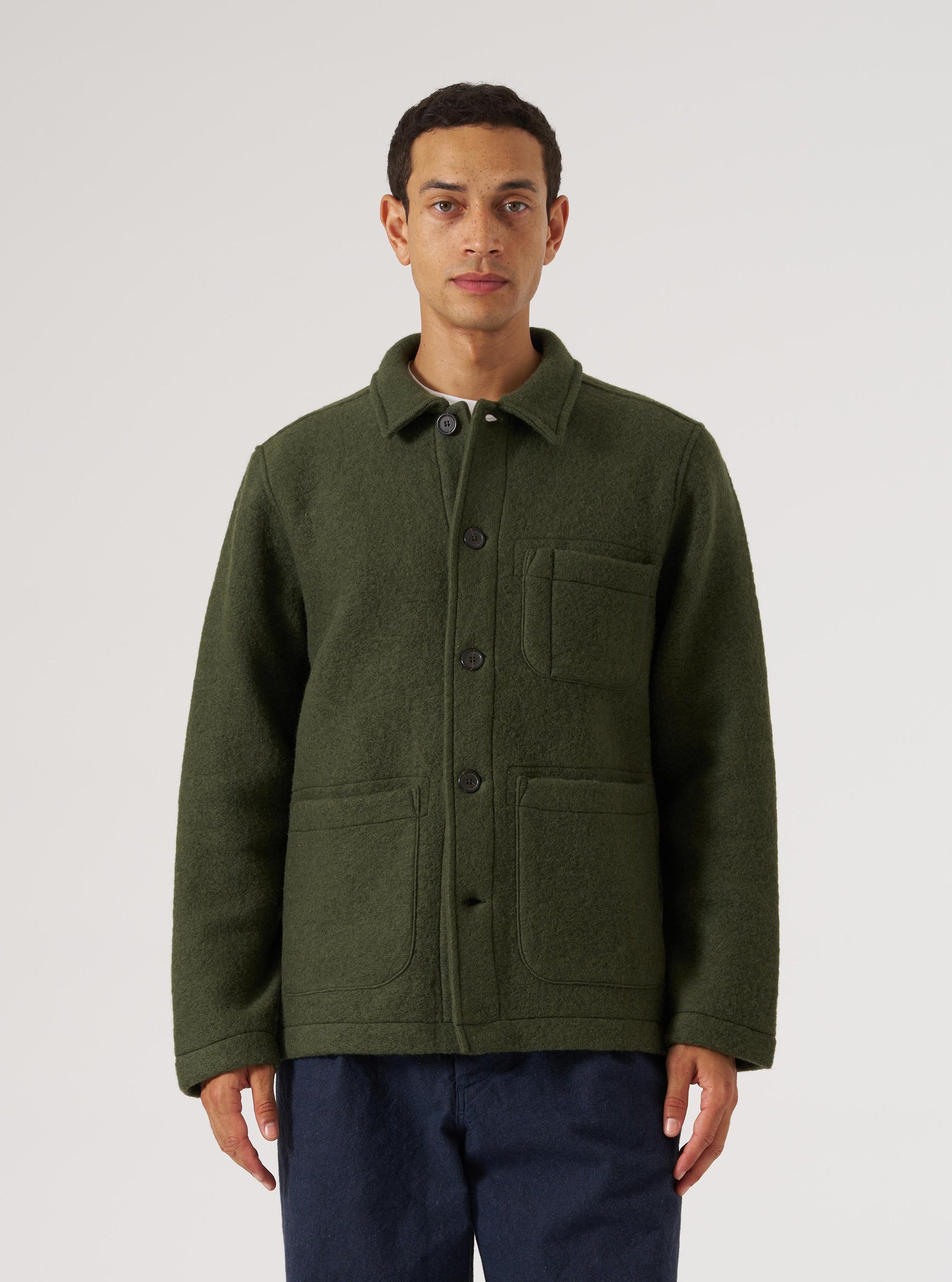 A man stands against a white backdrop wearing an Olive Wool Fleece Field Jacket. The jacket is buttoned and has pockets. He is also wearing navy pants.