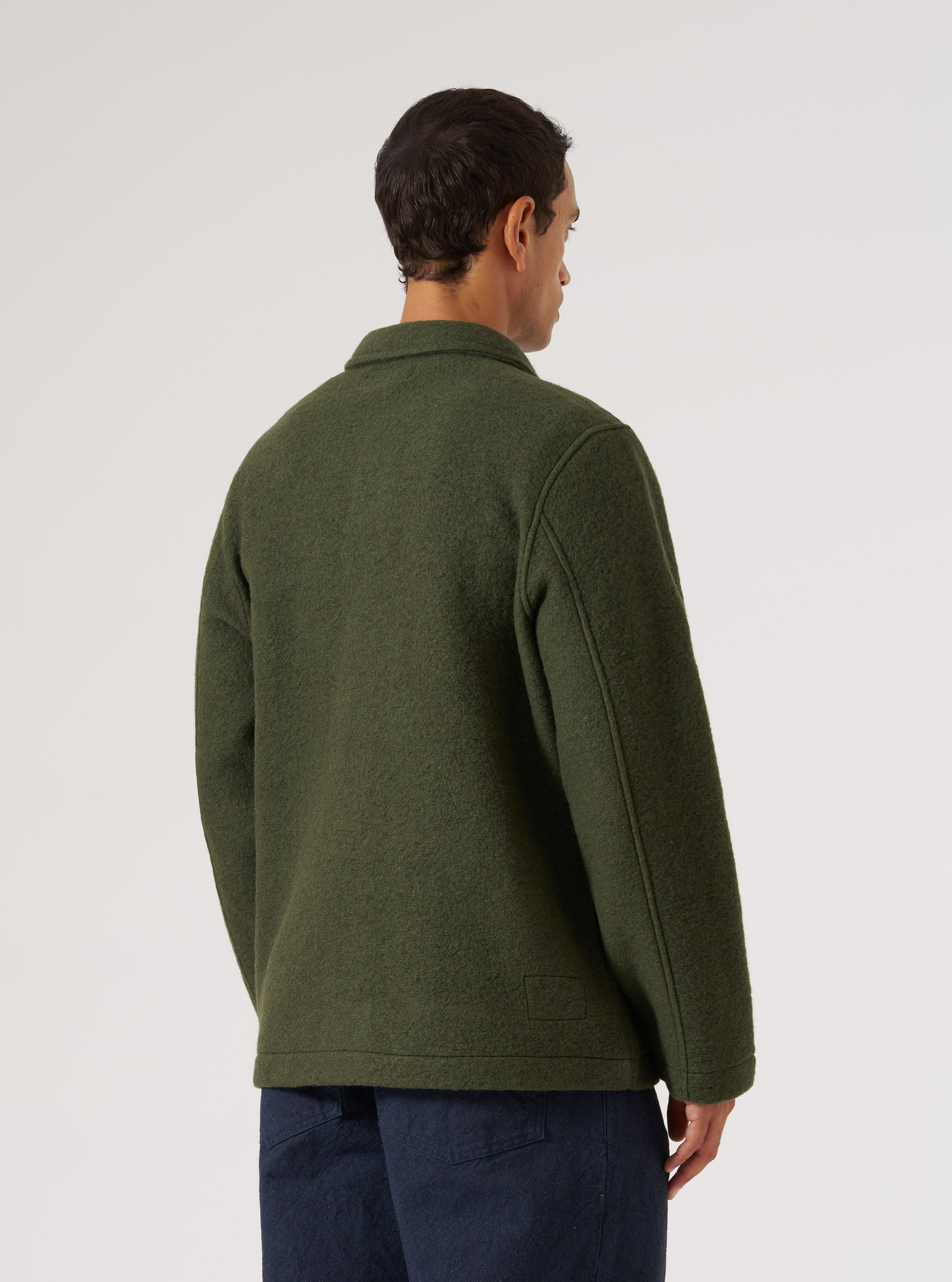 Back view of a man wearing the Olive Wool Fleece Field Jacket. The jacket is olive green and made of wool fleece. He is wearing dark blue pants. White background.