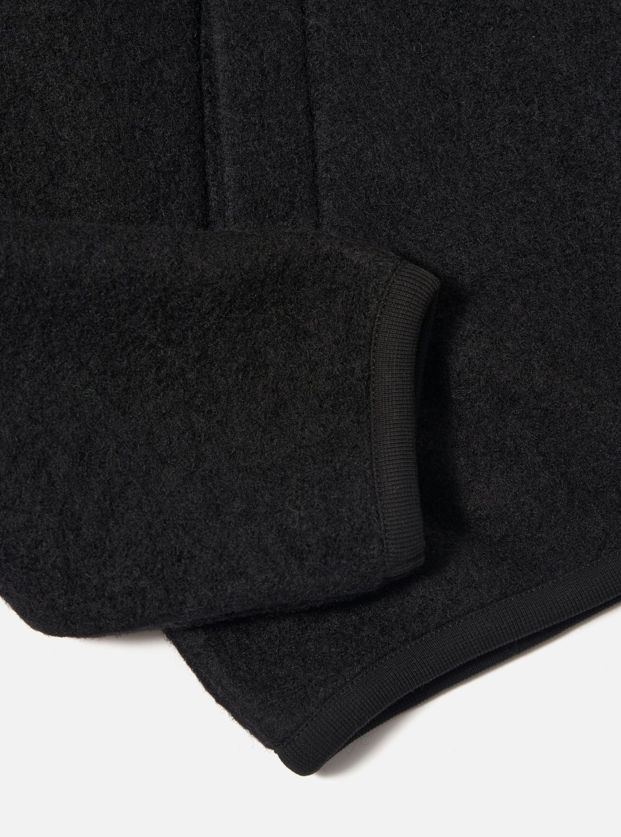 Close-up of the Black Wool Fleece Zip Bomber sleeve on a white background. The black wool fleece material is visible, along with the ribbed cuff.