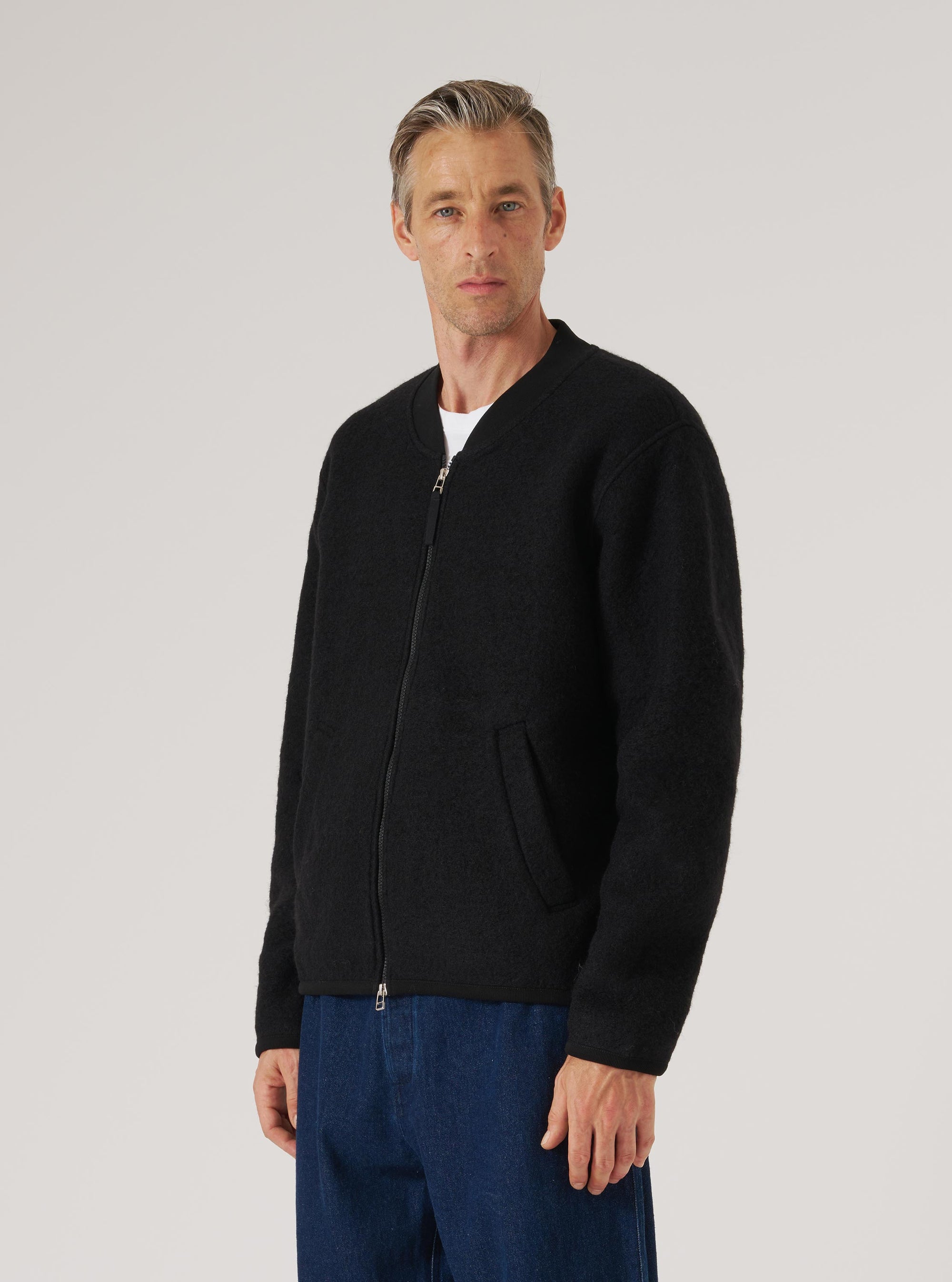 A model in a Black Wool Fleece Zip Bomber on a white background. The bomber is paired with blue jeans. The fleece has a visible texture.