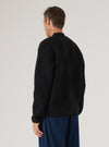 Back view of a model wearing a Black Wool Fleece Zip Bomber. The bomber is black and made of wool fleece. The background is a plain white studio backdrop.