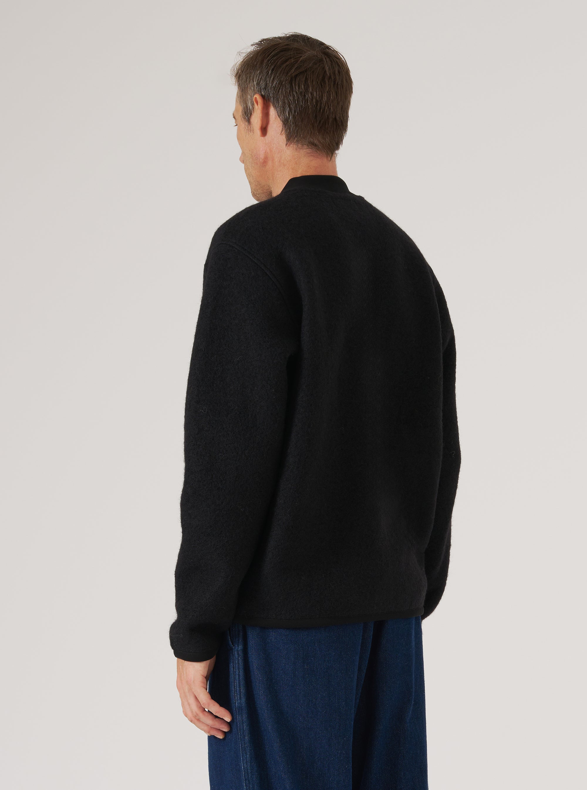 Back view of a model wearing a Black Wool Fleece Zip Bomber. The bomber is black and made of wool fleece. The background is a plain white studio backdrop.