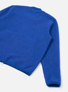 Blue wool fleece zip bomber laid flat on a light grey surface, shot from above at an angle. The image shows the back and one sleeve, highlighting the brushed wool fleece texture. A silver zip is visible at the lower left hem. Ribbed cuffs and hem trim contrast with the fluffy fleece body.