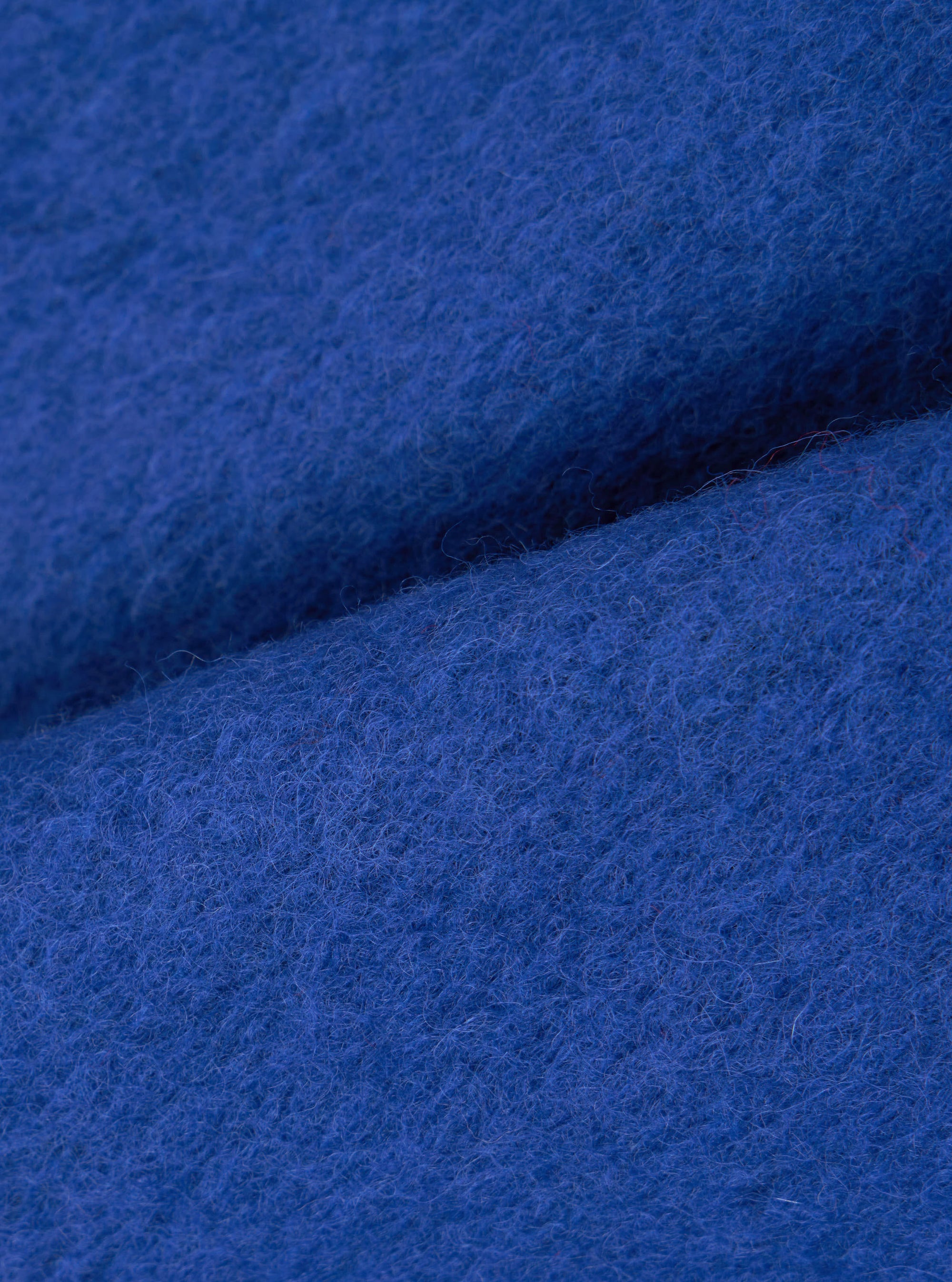 Close-up of the cobalt blue wool fleece fabric used in the zip bomber, showing the dense, lightly boiled texture with fine loose fibres on the surface. The fabric is folded to reveal its soft, brushed face and substantial weight. No garment details are visible.