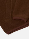 Close-up flat lay of a cacao wool fleece zip bomber on a white surface, showing the hem and sleeve cuff. The brushed wool fleece has a dense, slightly napped texture. A darker brown ribbed knit trim edges both the curved cuff opening and the straight hem. Vertical fold lines are visible across the body of the garment.