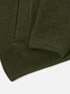 Close-up flat lay of an olive wool fleece zip bomber on a white surface. The boiled wool texture is visible across the body. A ribbed knit hem trim in matching olive runs along the bottom edge, with neat topstitching. A sleeve fold is visible in the upper portion of the frame.