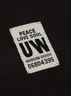 Close-up of the Black Single Jersey Core Tee showing the fabric and a tag with 'Peace Love Soul UW Modern Goods 06804395' on it. The tee is laid flat.