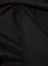 Close-up of the Black Single Jersey Core Tee fabric. The soft, single jersey material is draped to show texture. Dark, neutral background.