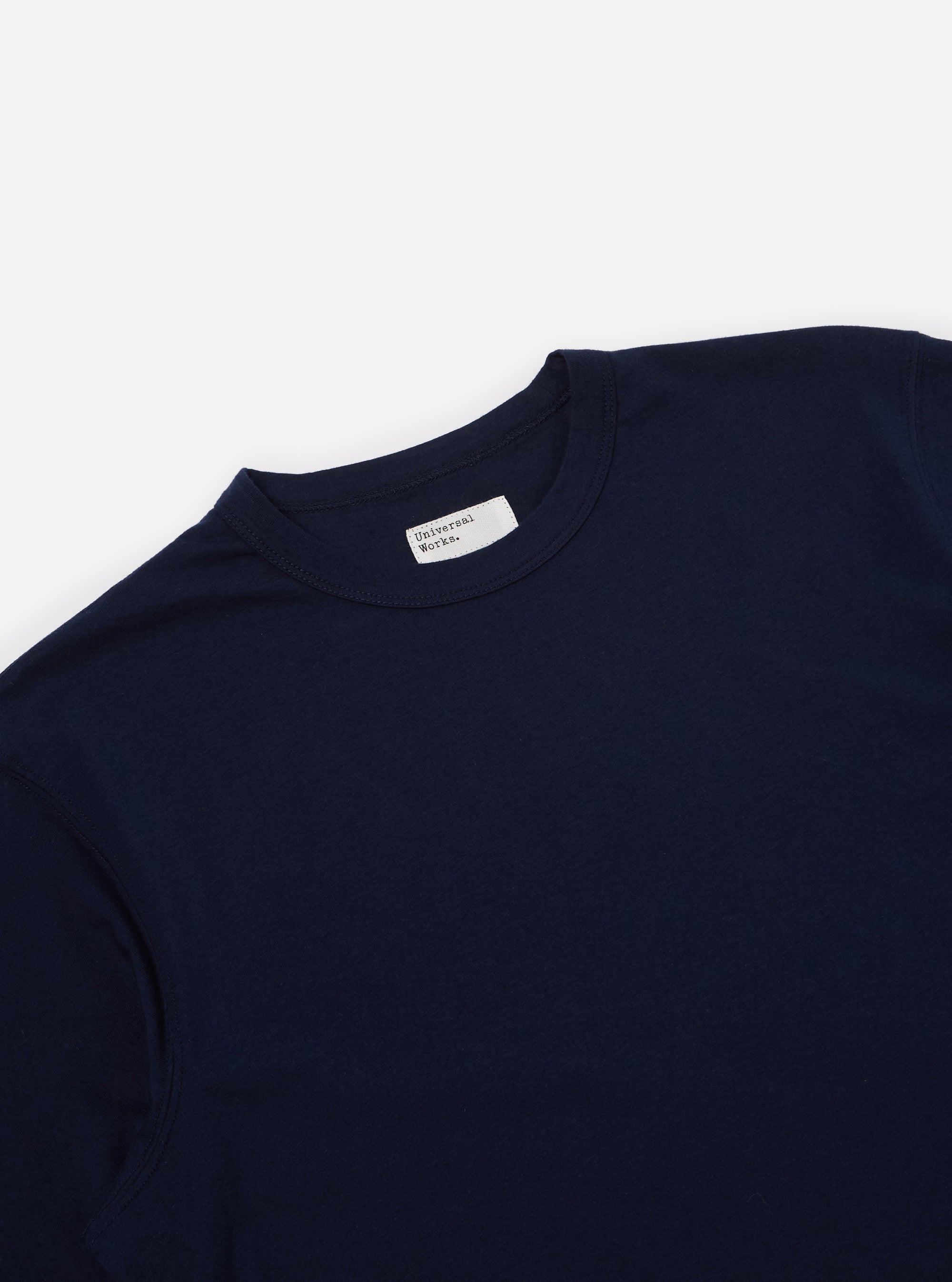 Close-up of the Navy Single Jersey Core Tee on a white surface. The tee is a dark navy color and made of a soft, single jersey material. The fit is relaxed and comfortable.