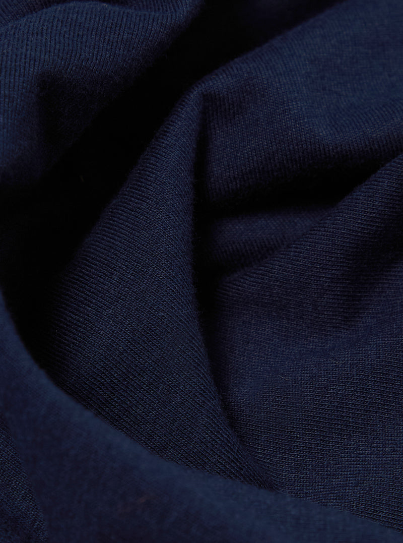 Close-up of the Navy Single Jersey Core Tee fabric. The soft, textured material is draped on a flat surface, showcasing its rich navy color and fine knit.