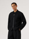 A model poses in a Black Wool Fleece Zip Liner Jacket against a white backdrop. The jacket is black wool fleece with a zip front and pockets.