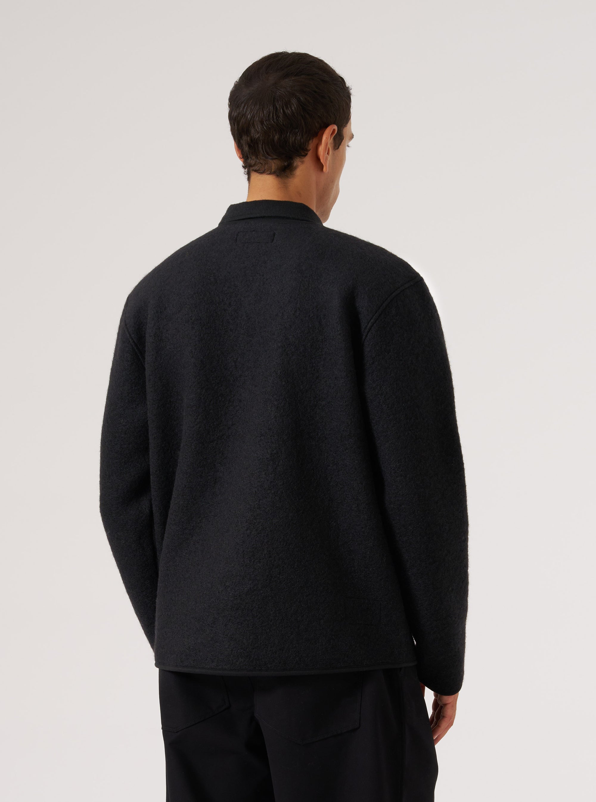 Back view of a model wearing a Black Wool Fleece Zip Liner Jacket against a white backdrop. The jacket is black wool fleece with a zip liner.