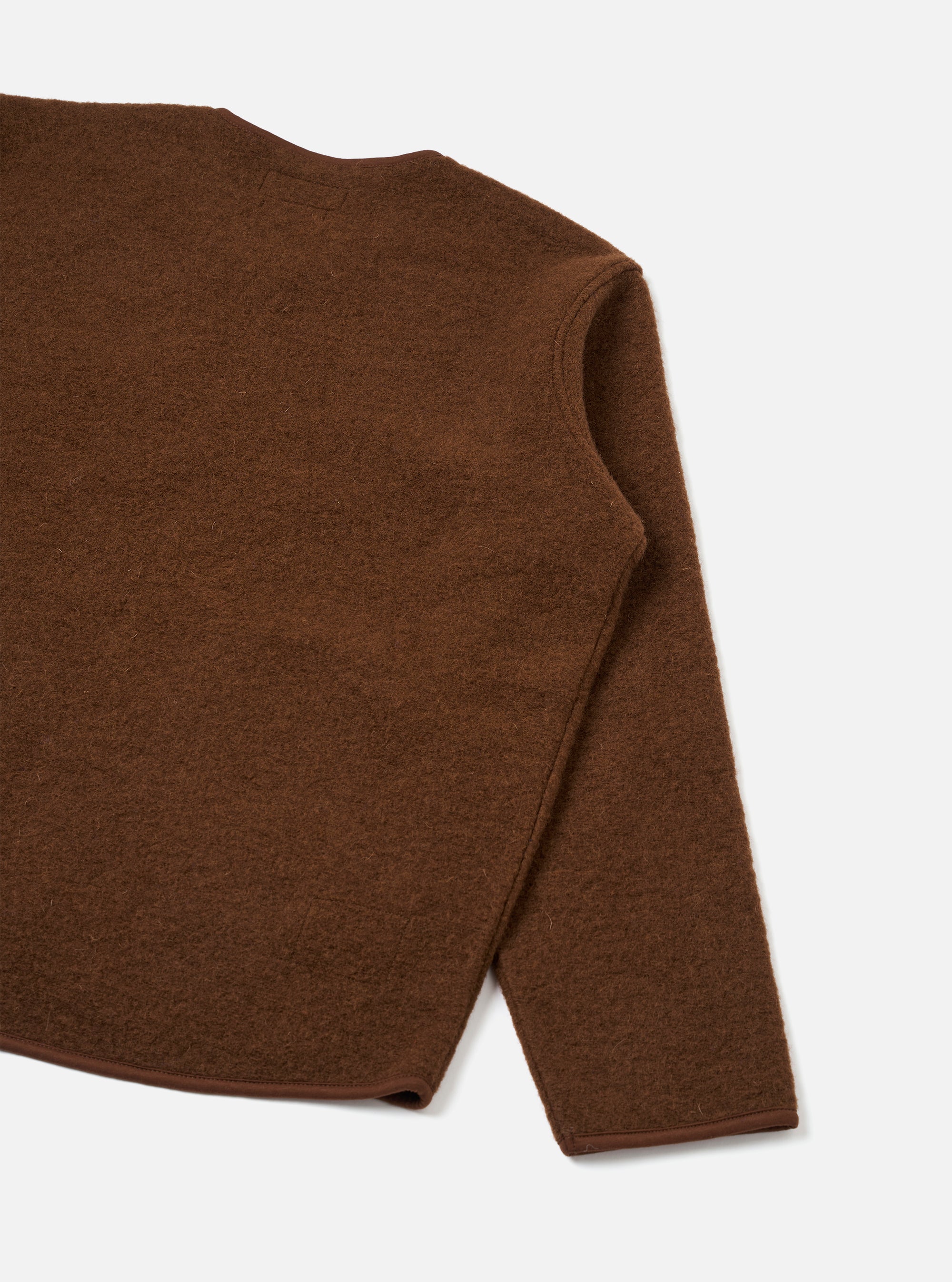 Close-up flat lay of a cacao brown wool fleece zip liner jacket on a light grey seamless backdrop. The shot captures the upper back, right shoulder seam and one full sleeve. The boiled wool fleece has a lightly textured, brushed surface. A narrow bound hem edge is visible at the sleeve and bottom.