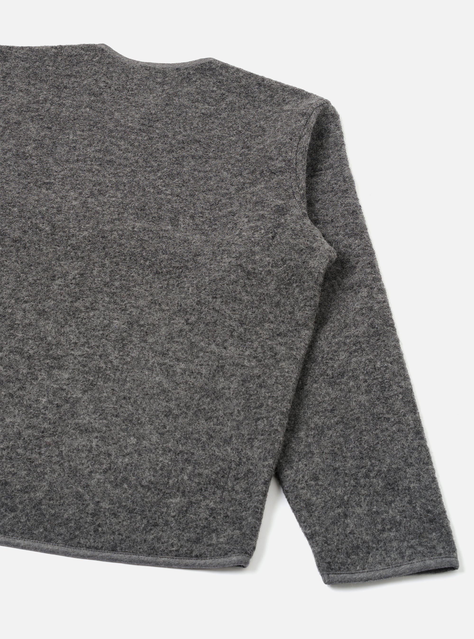 Grey marl wool fleece zip liner jacket, flat lay on a white studio backdrop. Shot shows the back and right sleeve at close range. The boiled wool fleece texture is visible across the body and sleeve. A contrast bound hem runs along the bottom edge. The round neckline is partially visible at the top.