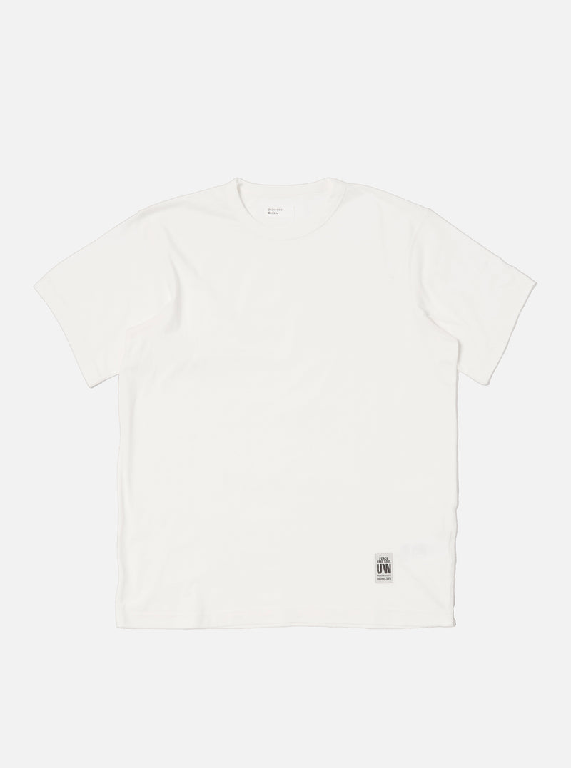 Flat lay of an Ecru Single Jersey Core Tee on a white background. The tee is a light cream color and has a relaxed fit. A small tag is visible near the hem.