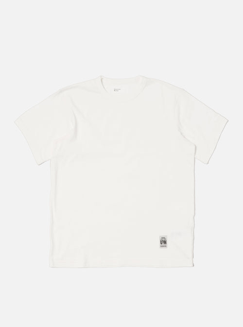 Flat lay of an Ecru Single Jersey Core Tee on a white background. The tee is a light cream color and has a relaxed fit. A small tag is visible near the hem.