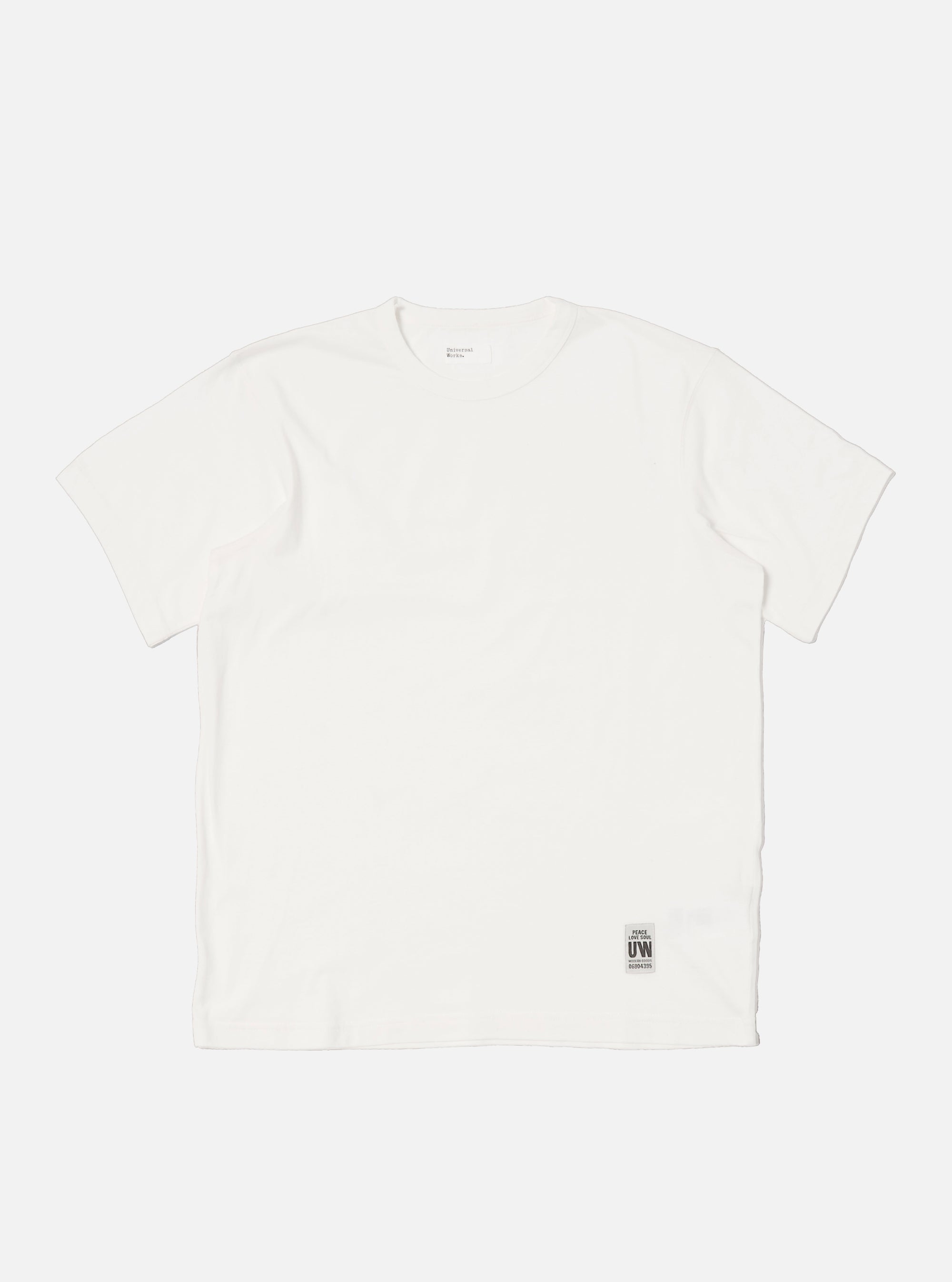 Flat lay of an Ecru Single Jersey Core Tee on a white background. The tee is a light cream color and has a relaxed fit. A small tag is visible near the hem.