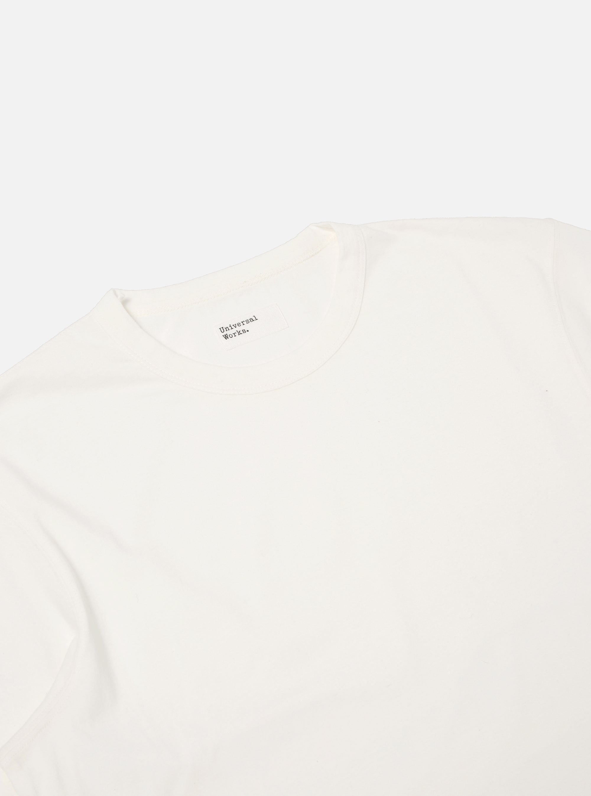 Close-up of the Ecru Single Jersey Core Tee on a white background. The soft, neutral color and smooth fabric are highlighted. The brand label is visible at the neck.