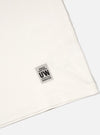 Close-up of the Ecru Single Jersey Core Tee on a white surface, showing the fabric texture and UW label. The tee has a classic, comfortable fit.