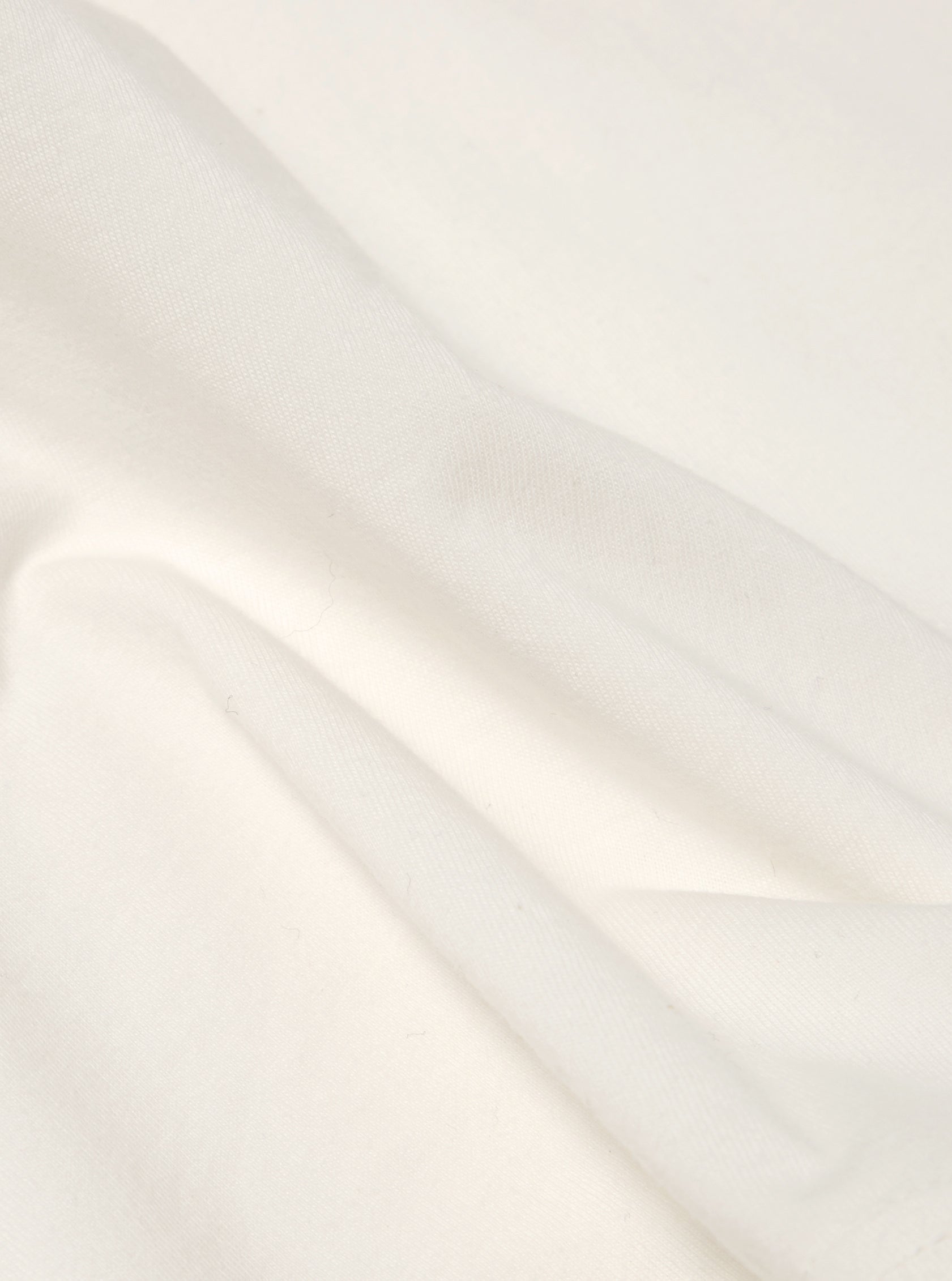 Close-up of the Ecru Single Jersey Core Tee fabric. Soft, off-white cotton with subtle folds. Studio shot on a plain background.