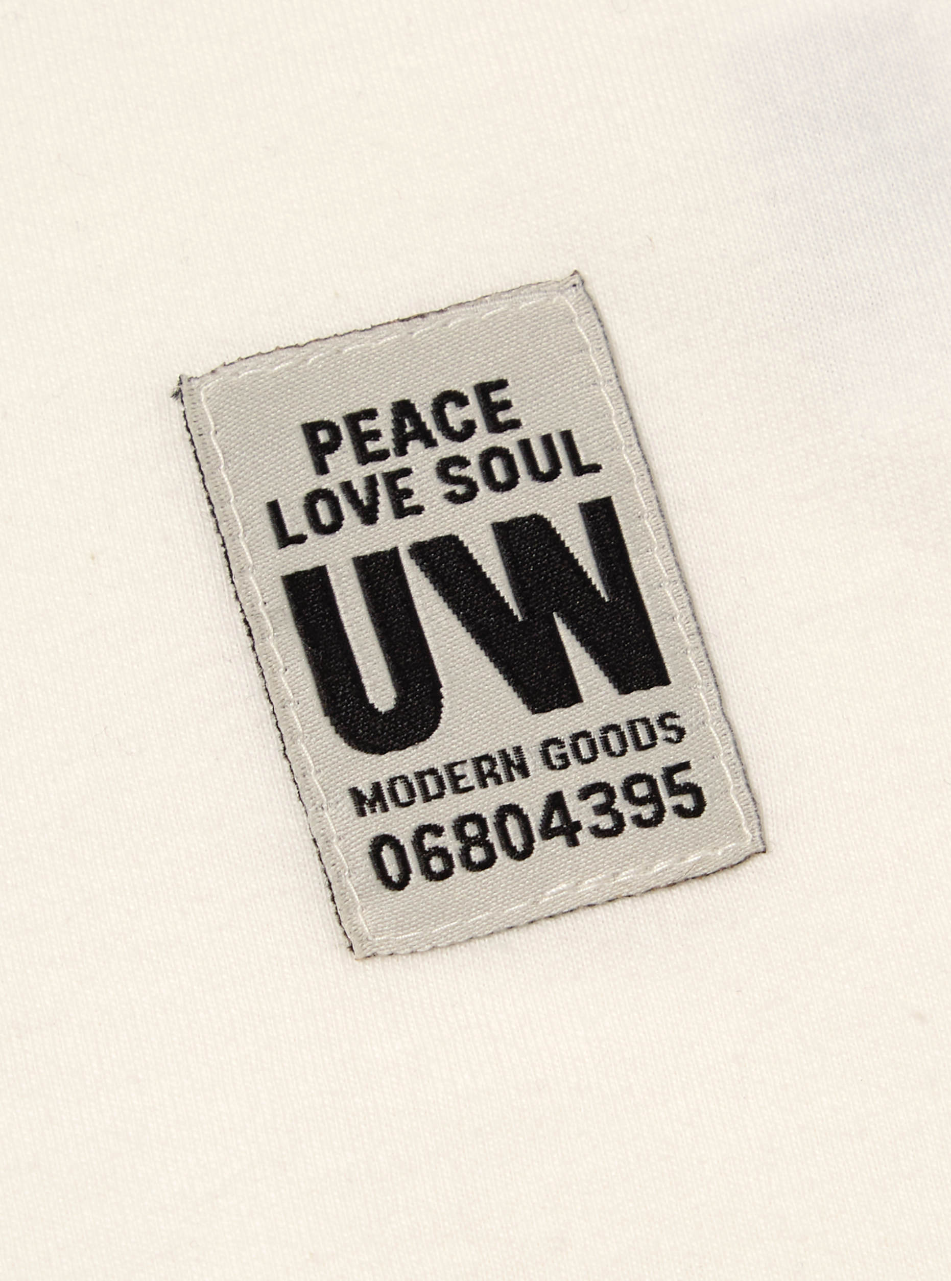 Close up of the label on the Ecru Single Jersey Core Tee. The label is gray with black text. The tee is ecru.