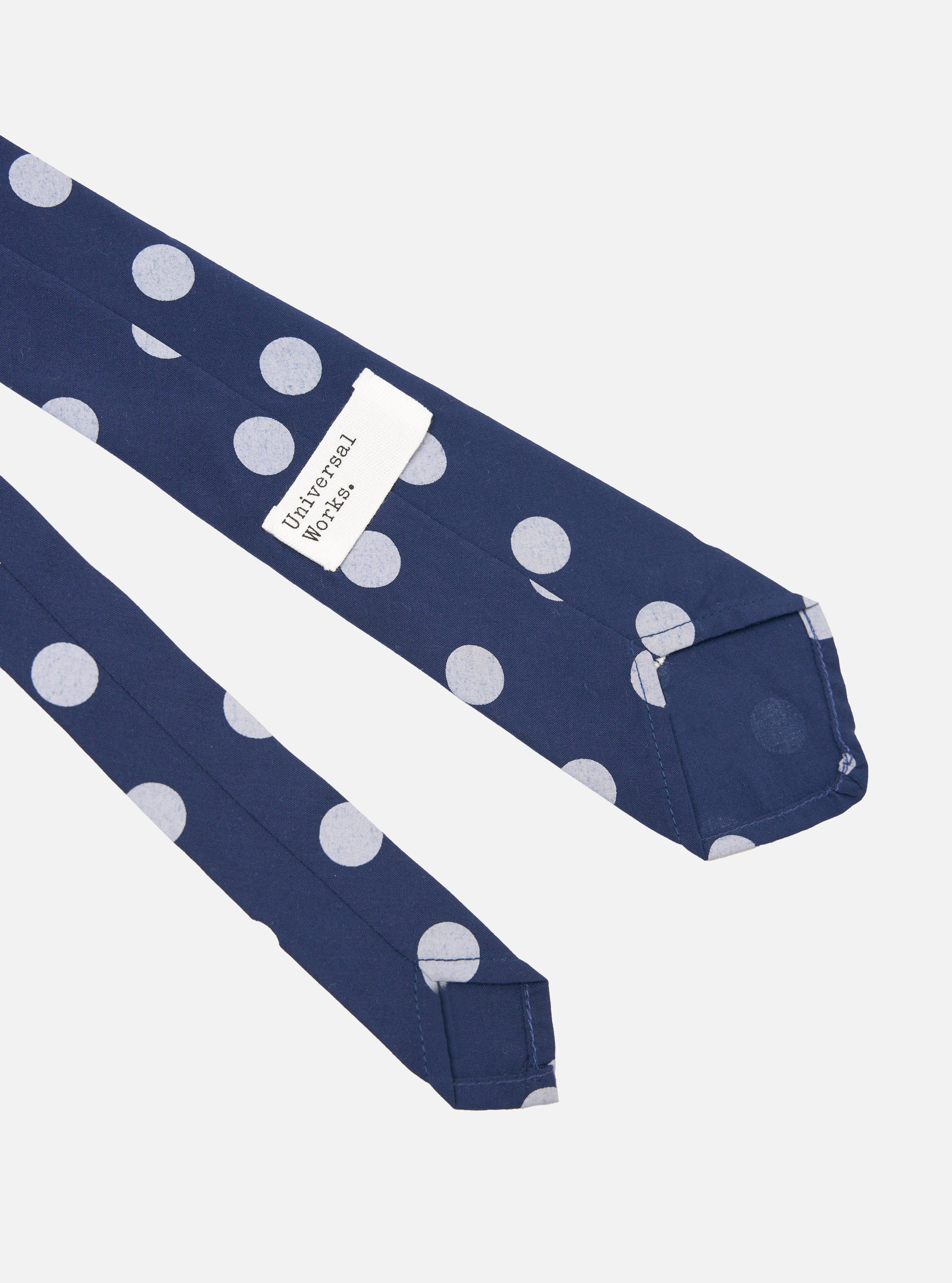 Close-up of a Navy Bold Dot Print Rayon Tie on a white background. The tie features large white polka dots and a 'Universal Works' tag.
