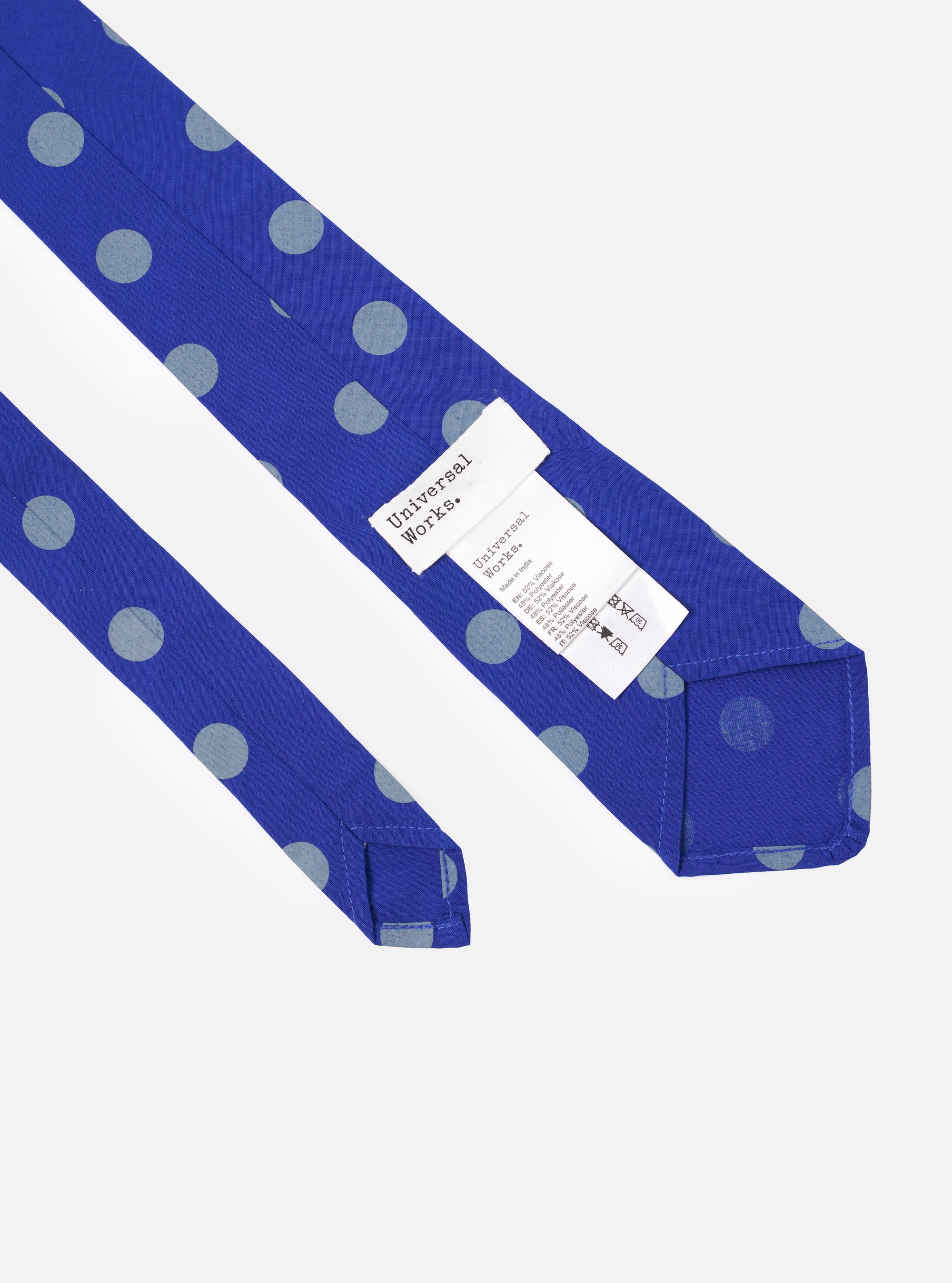 The Blue Bold Dot Print Rayon Tie is shown in a detail shot as a flat lay against a plain white background. The tie features a deep blue base with a repeating pattern of large, white bold dots. The smooth, slightly lustrous texture of the rayon fabric is visible in the close-up view.