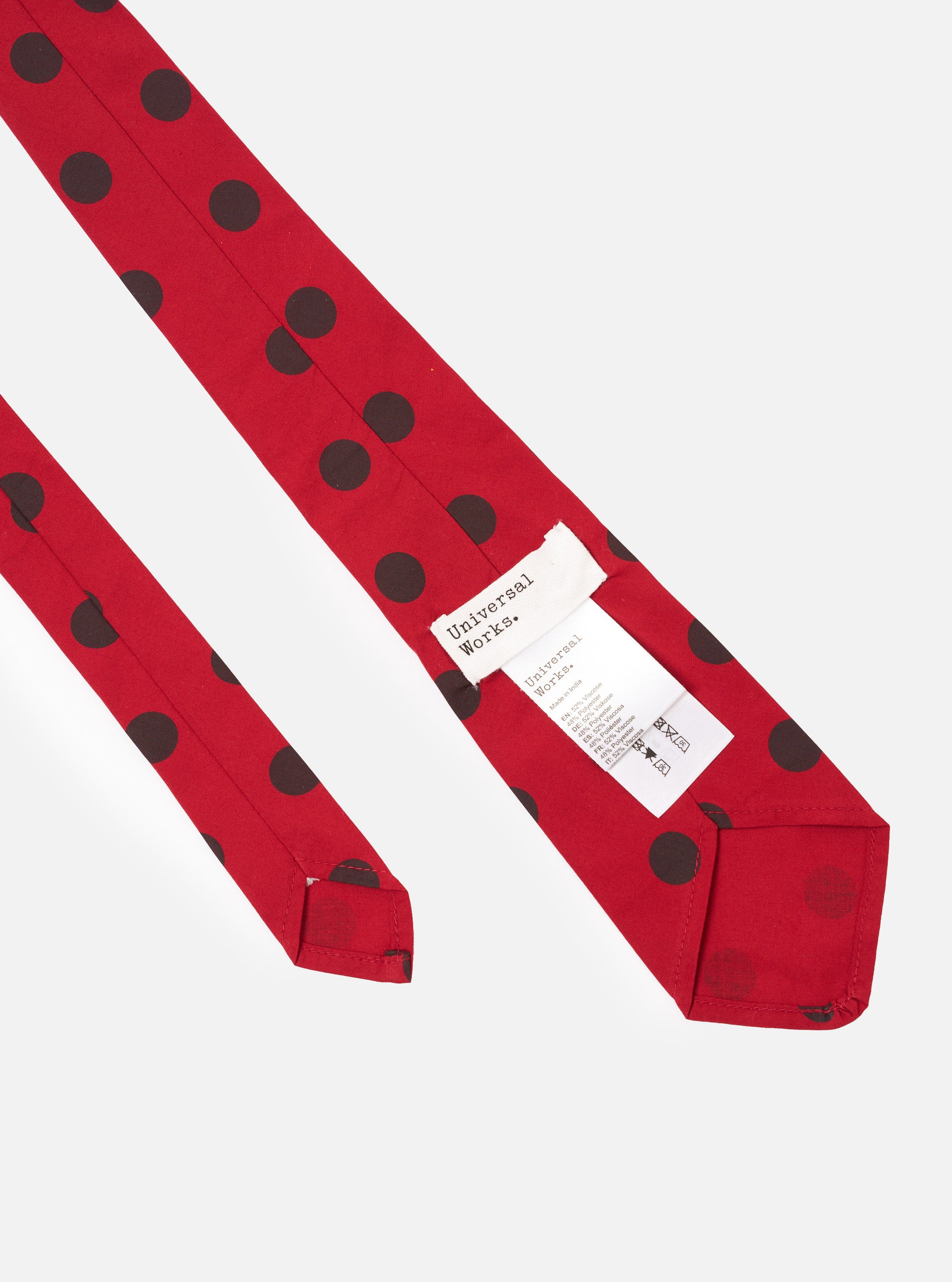 The Red/Black Bold Dot Print Rayon Tie is shown from a rear angle as a flat lay against a plain white background. The image highlights the tie's construction, showing the keeper loop and the tipped end featuring the bold red and black polka dot pattern. The smooth texture of the rayon fabric is visible.