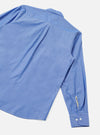 Blue chambray Daybrook shirt laid flat on a light grey seamless backdrop, shot from above at an angle. The back yoke, point collar and one long sleeve are visible. The buttoned cuff shows two white buttons, with a cream contrast placket detail at the sleeve opening.