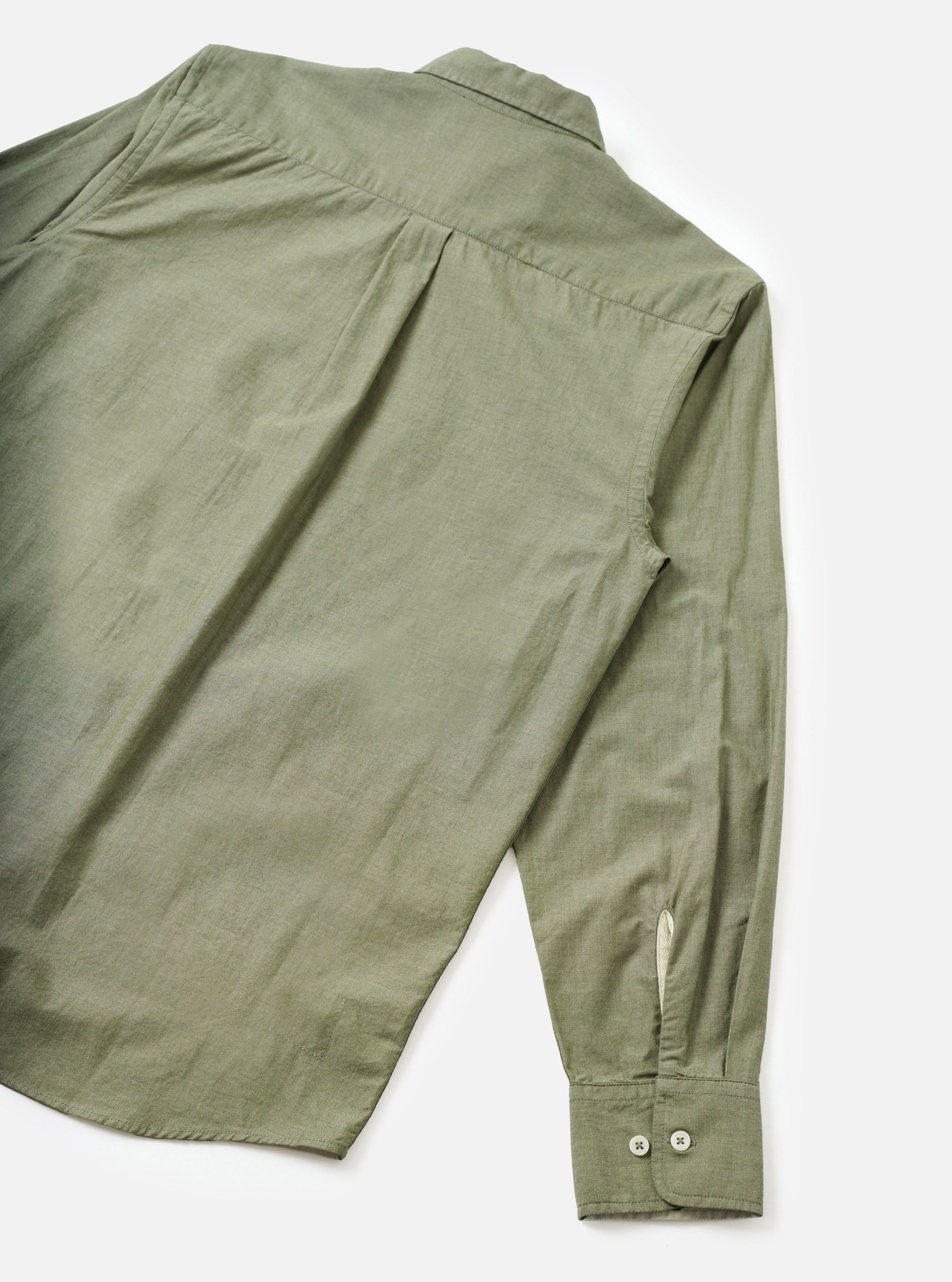 Flat lay of an olive chambray shirt on a white background, shot from the back. Visible details include a back yoke with a centre pleat, one long sleeve extending to the lower right, and a buttoned cuff with two small buttons and a gauntlet placket. The fabric has a fine chambray texture.