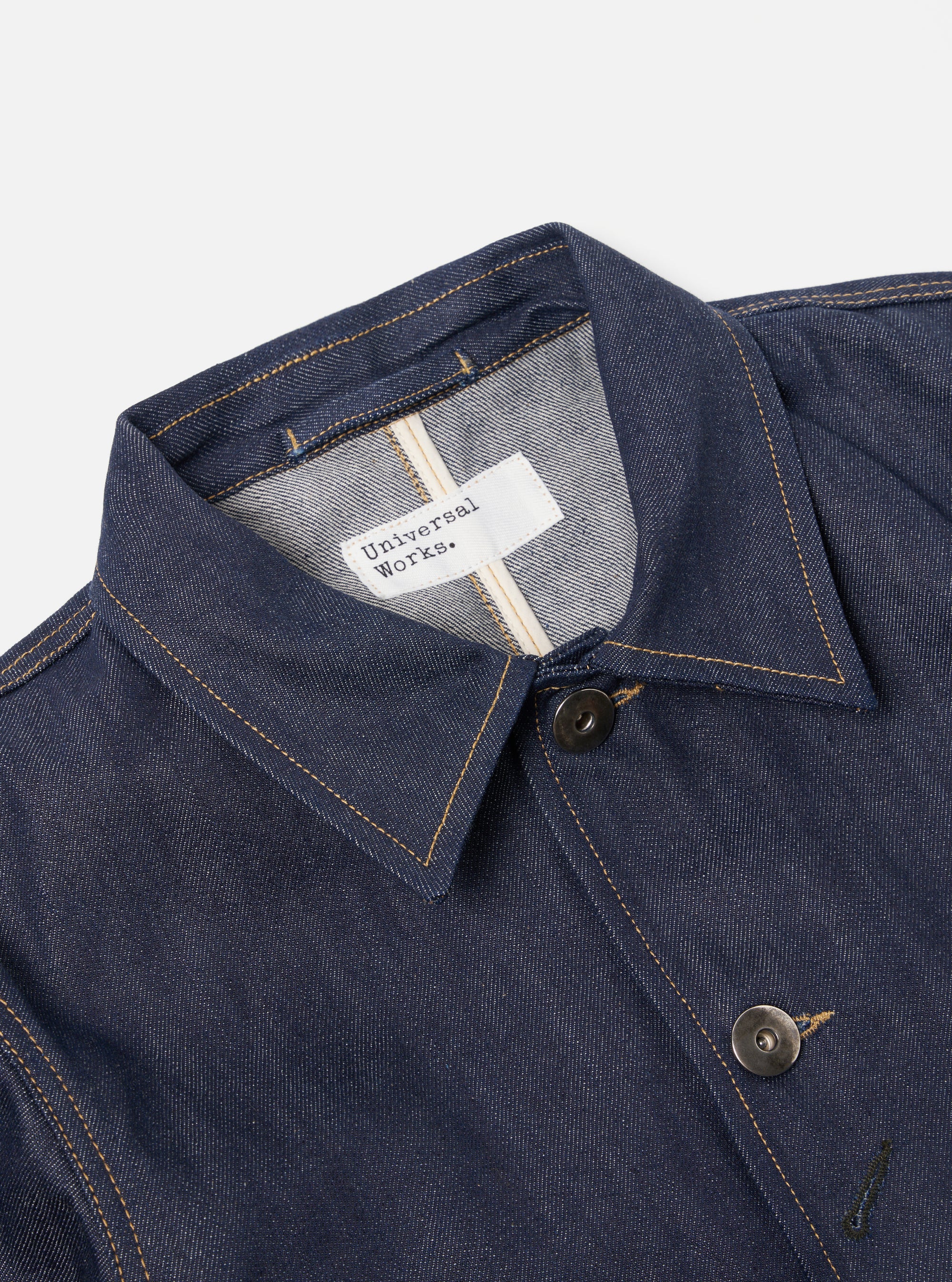 Close-up of the Indigo 13oz Selvedge Denim Bakers Jacket on a white background. Shows the jacket's collar, buttons, and stitching details.