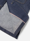 Close-up of the Indigo 13oz Selvedge Denim Bakers Jacket on a white surface. Shows the denim texture, red selvedge detail, and tan stitching. 