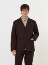 A male model stands against a plain white background wearing the Brown Twill Three Button Jacket. The jacket is a rich brown color with a textured twill weave, featuring a three-button front closure and three large patch pockets. It has a relaxed, unstructured fit with notched lapels and is paired with matching brown trousers for a complete tailored look.