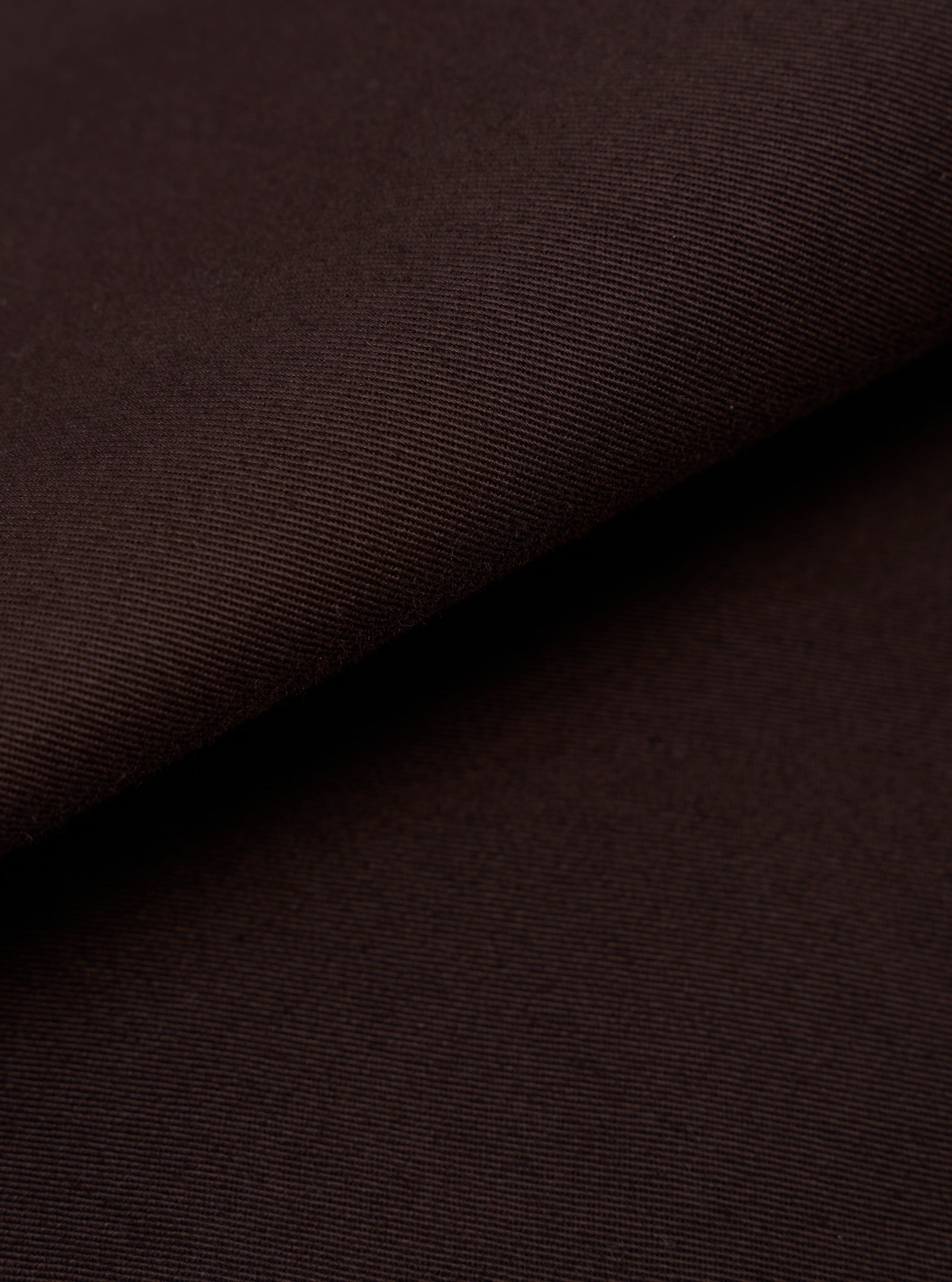 A detailed, close-up fabric swatch of the Brown Twill Three Button Jacket shows the intricate diagonal weave of the brown cotton material. The image highlights the texture and uniform earthy tone of the fabric against a neutral background.