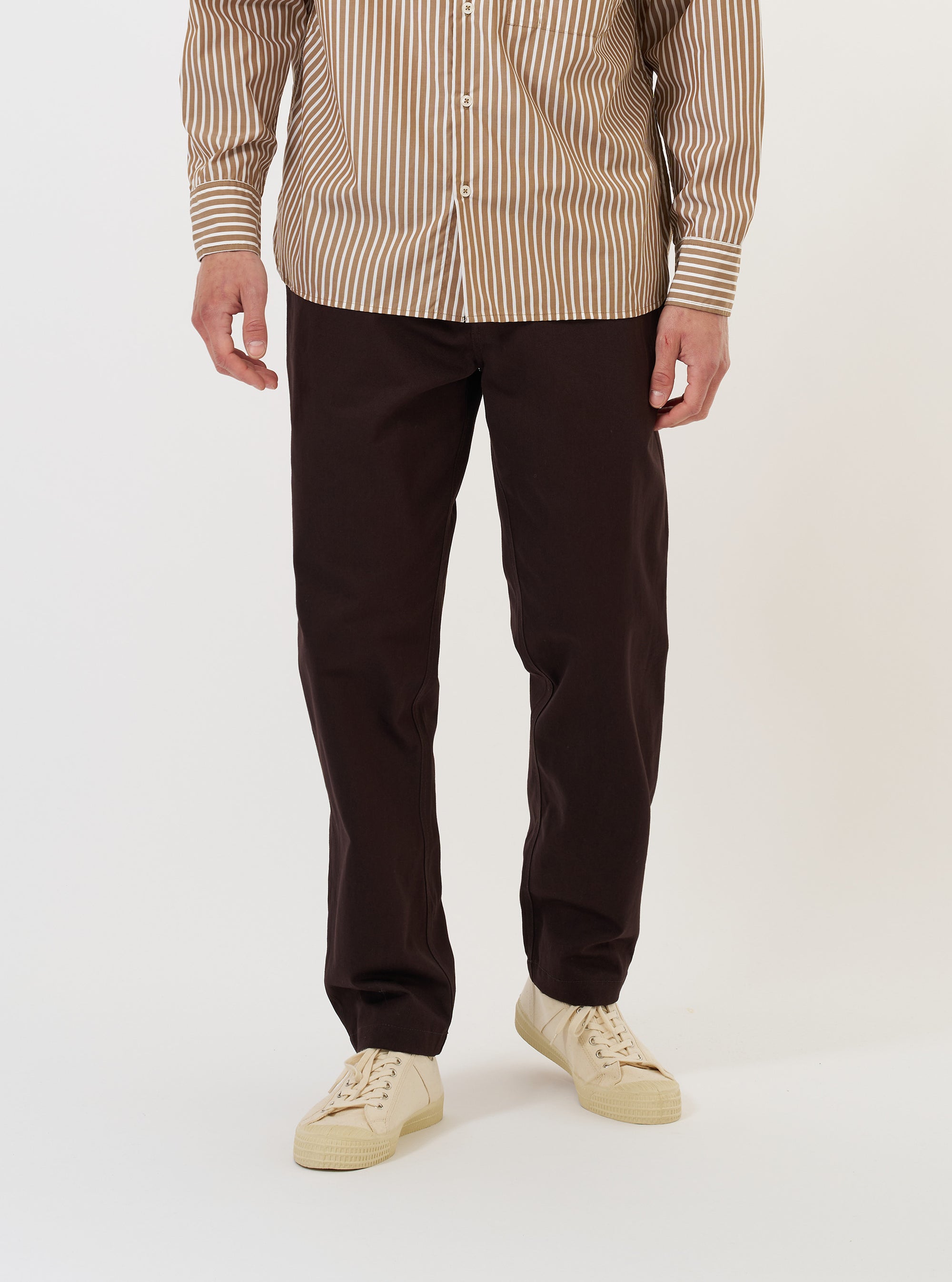 A model is wearing the Brown Twill Military Chino against a plain white background. The brown trousers feature a straight leg and are shown from the waist down, paired with dark footwear. The image highlights the fit and the durable cotton twill fabric of the chinos.