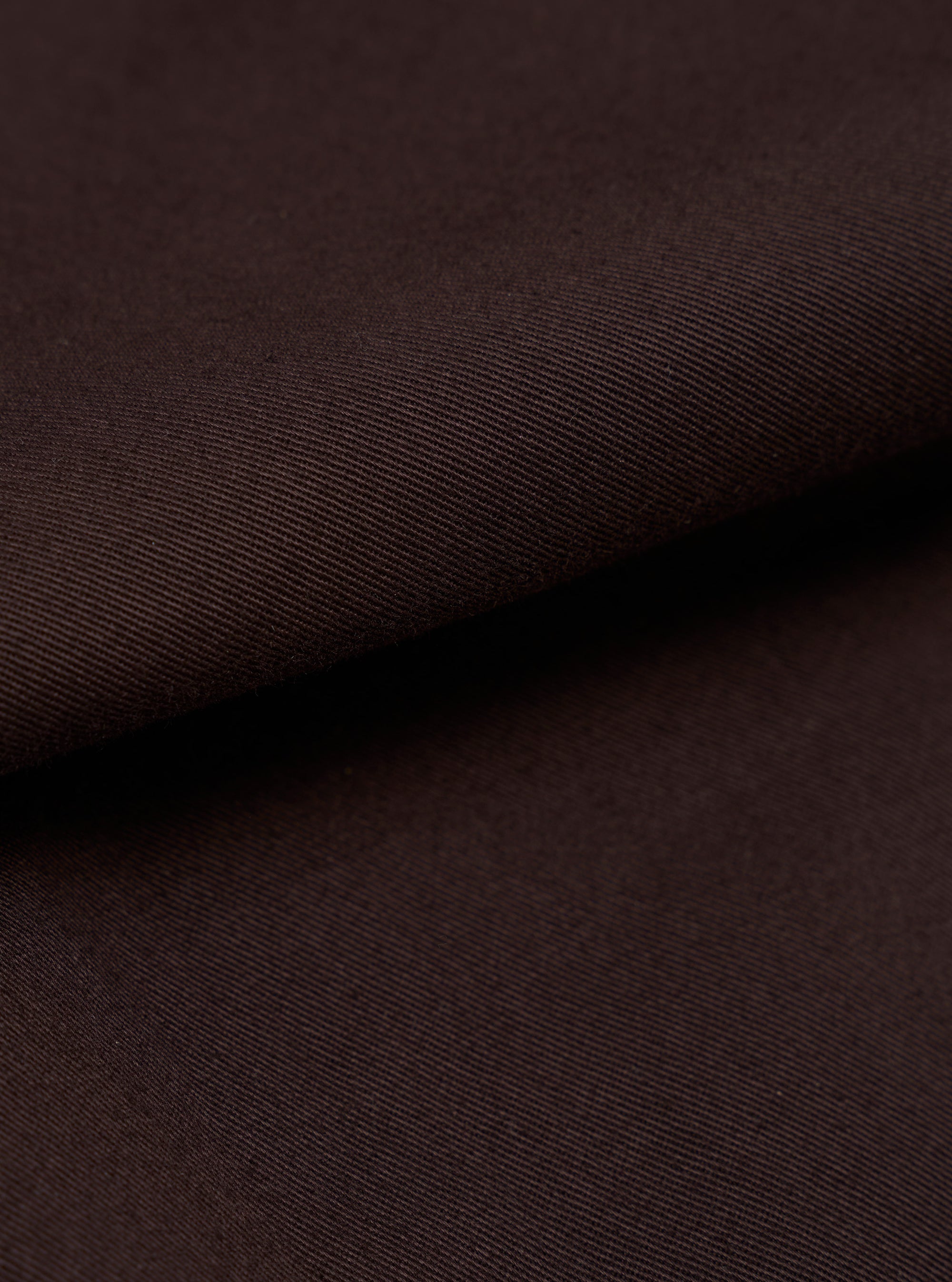 A detailed, close-up fabric swatch of the Brown Twill Military Chino is shown, highlighting the distinct diagonal 3/1 weave of the brown cotton material. The image focuses entirely on the texture and color of the fabric against a neutral background.