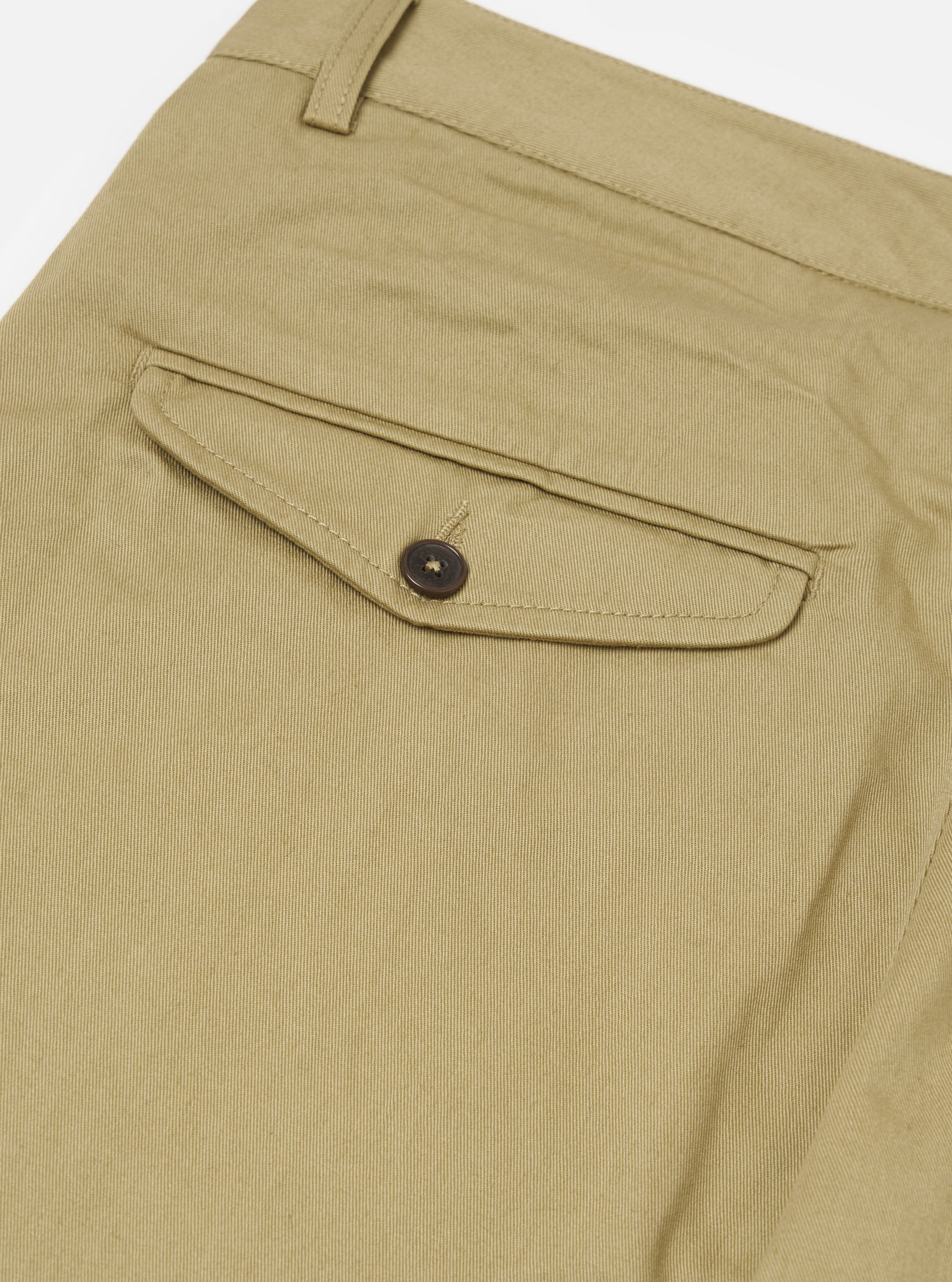Close-up of the Sand Twill Curved Pant, showcasing the twill texture and back pocket detail with button closure. Shot on a white surface.