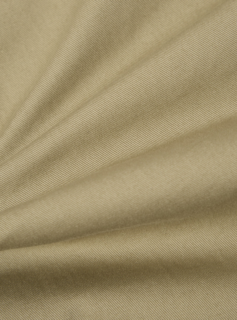 Close-up of the Sand Twill Aston Pant fabric. The twill weave is visible in the sand-colored material, draped on a flat surface.