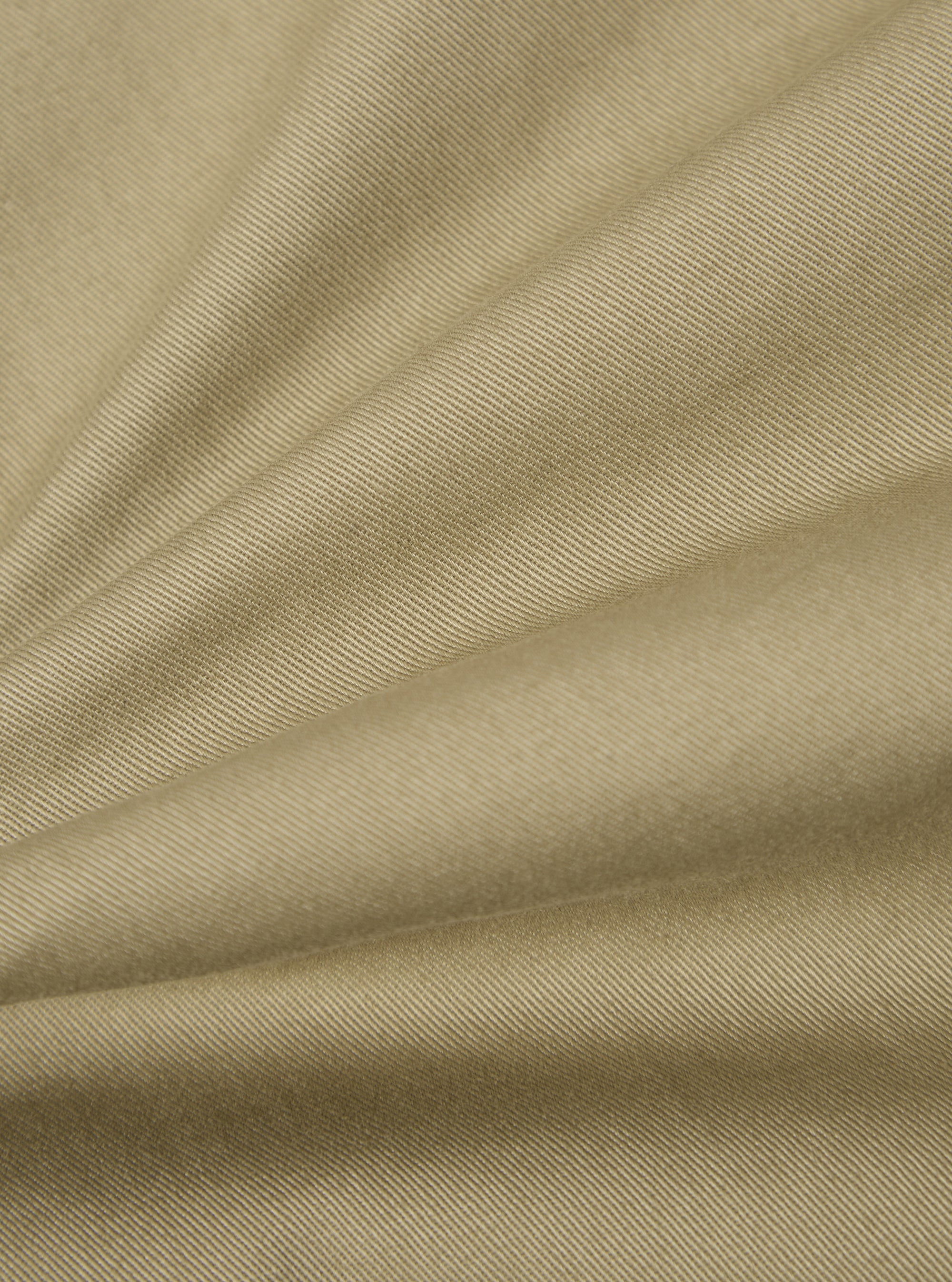 Close-up of the Sand Twill Aston Pant fabric. The twill weave is visible in the sand-colored material, draped on a flat surface.