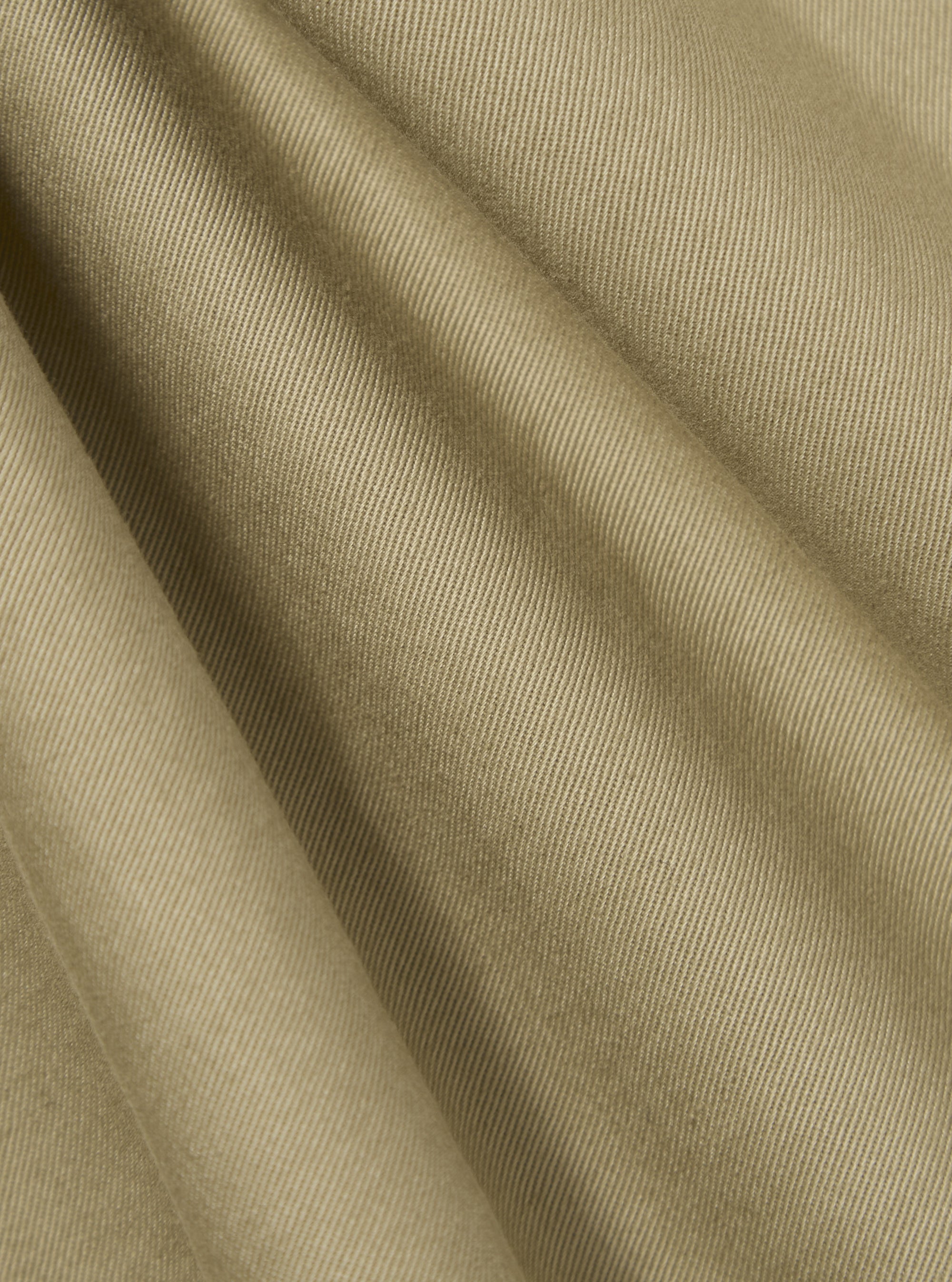 Close-up of the sand twill pleated track pant fabric. The material is a light tan color with a subtle ribbed texture. The fabric is draped to show its soft, flowing quality.