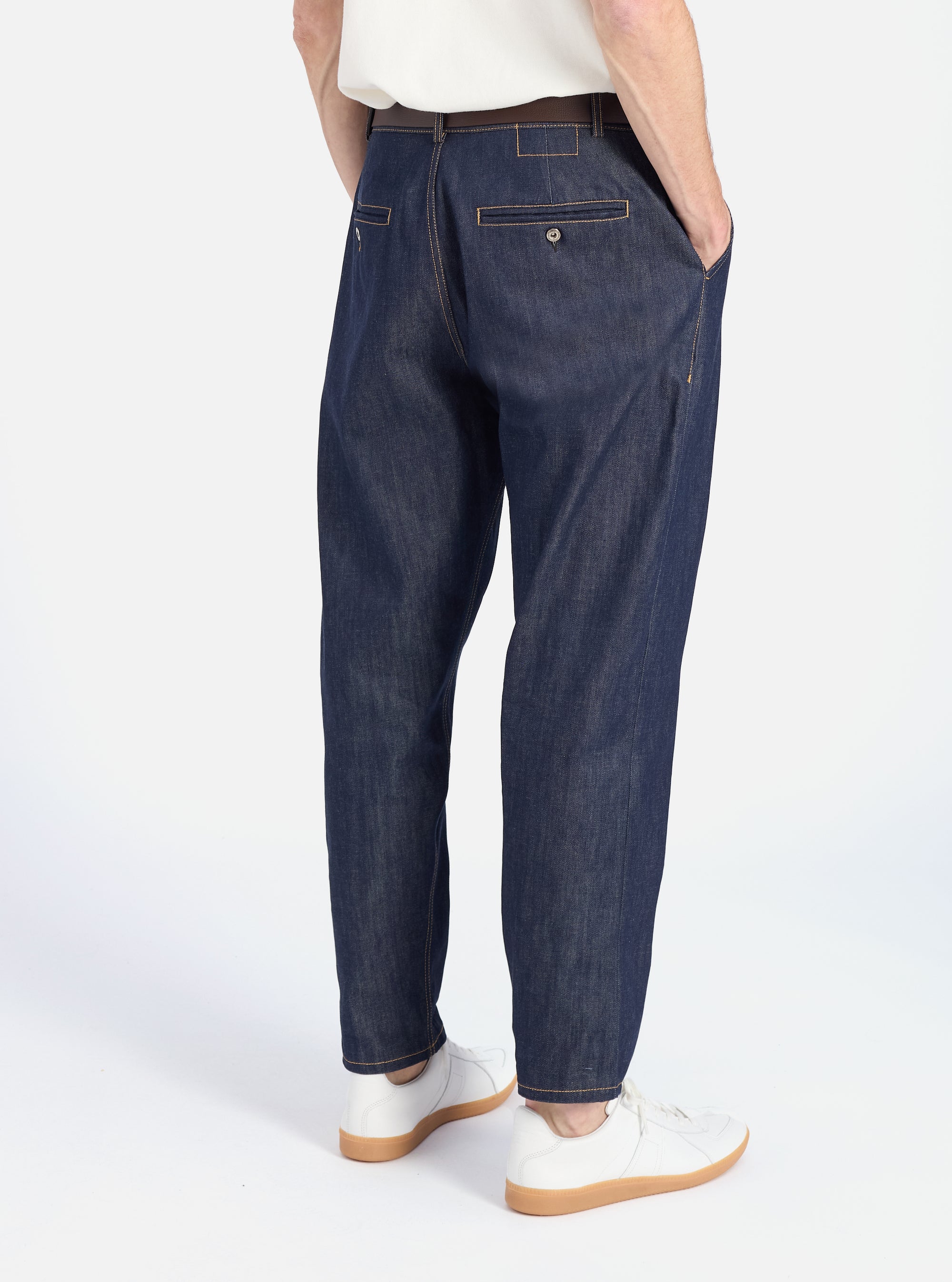 Back view of a model wearing Indigo 13oz Selvedge Denim Military Chino, dark blue denim pants with a relaxed fit. Shot in a white studio with white sneakers.